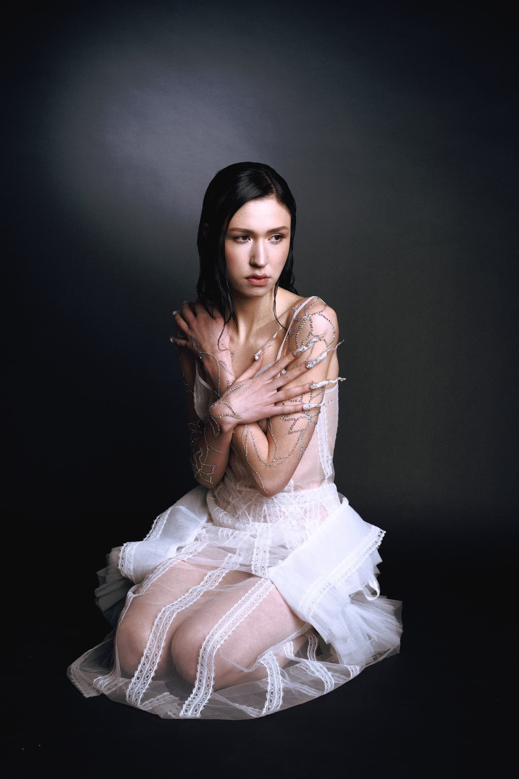 Woman in delicate white dress with jewelry art, set against dark background.