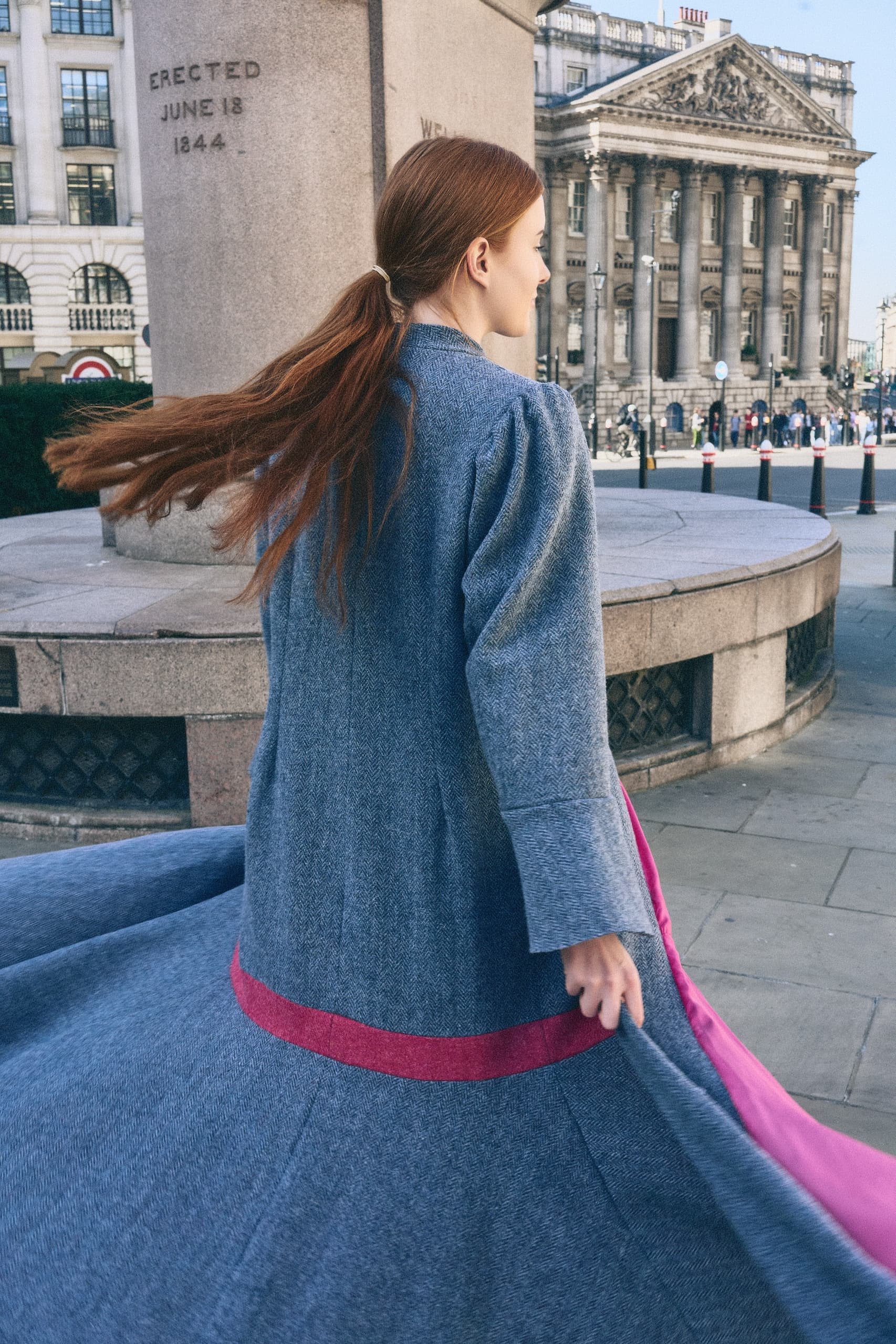Woman twirls in a stylish coat by a historic monument in the city.