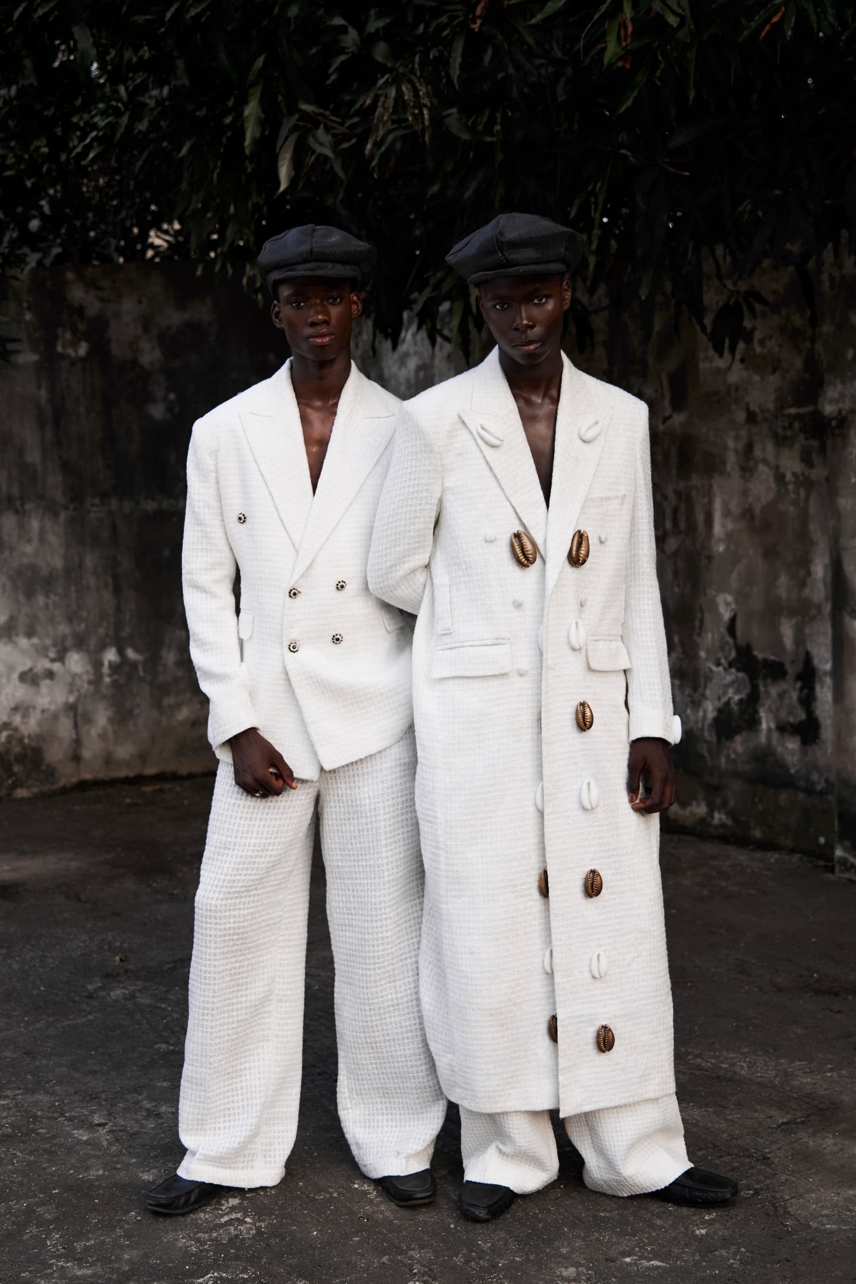 Two models in stylish white outfits and caps standing outdoors.