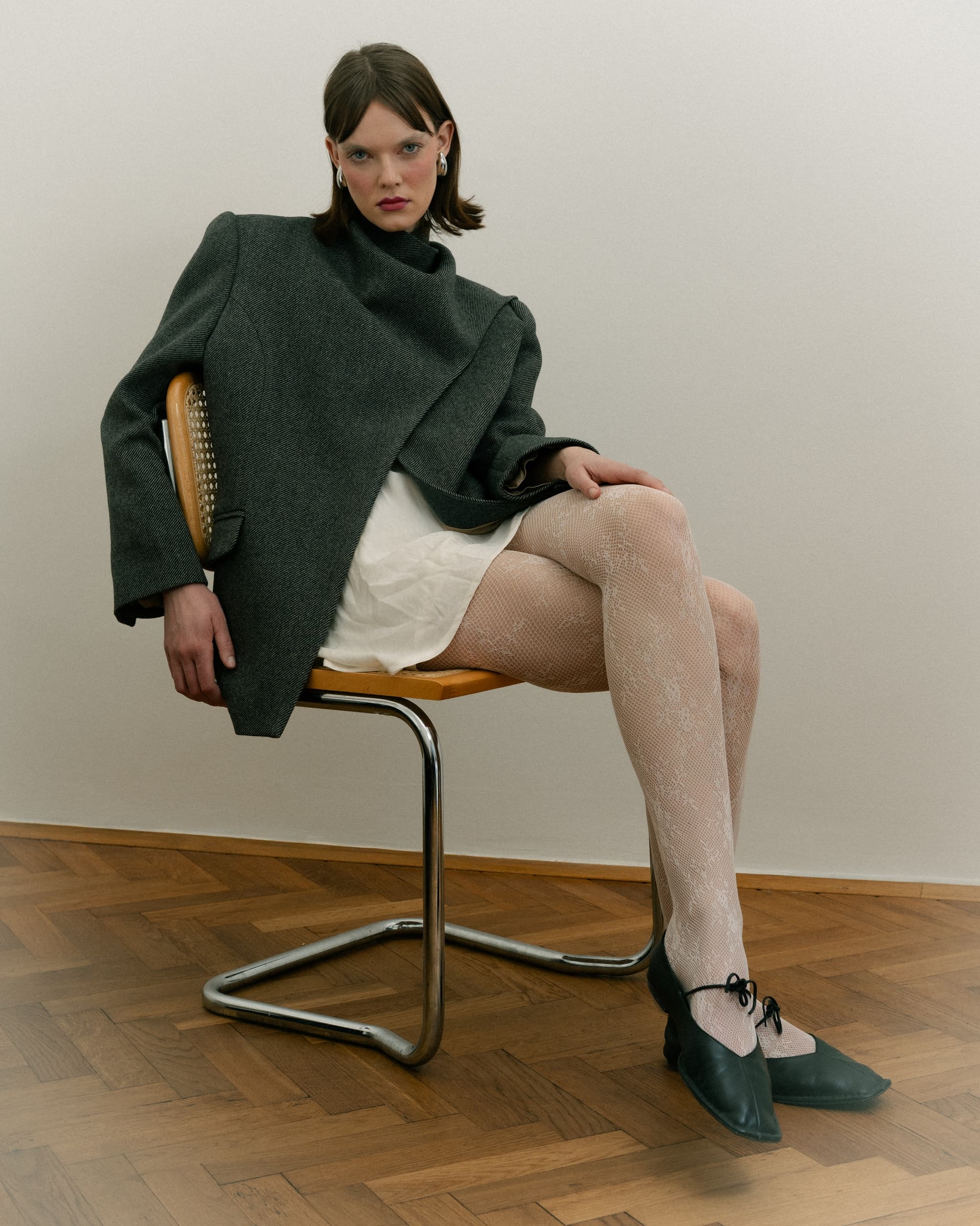 Fashionable woman in a chic outfit seated on a wooden chair in a minimalist room.