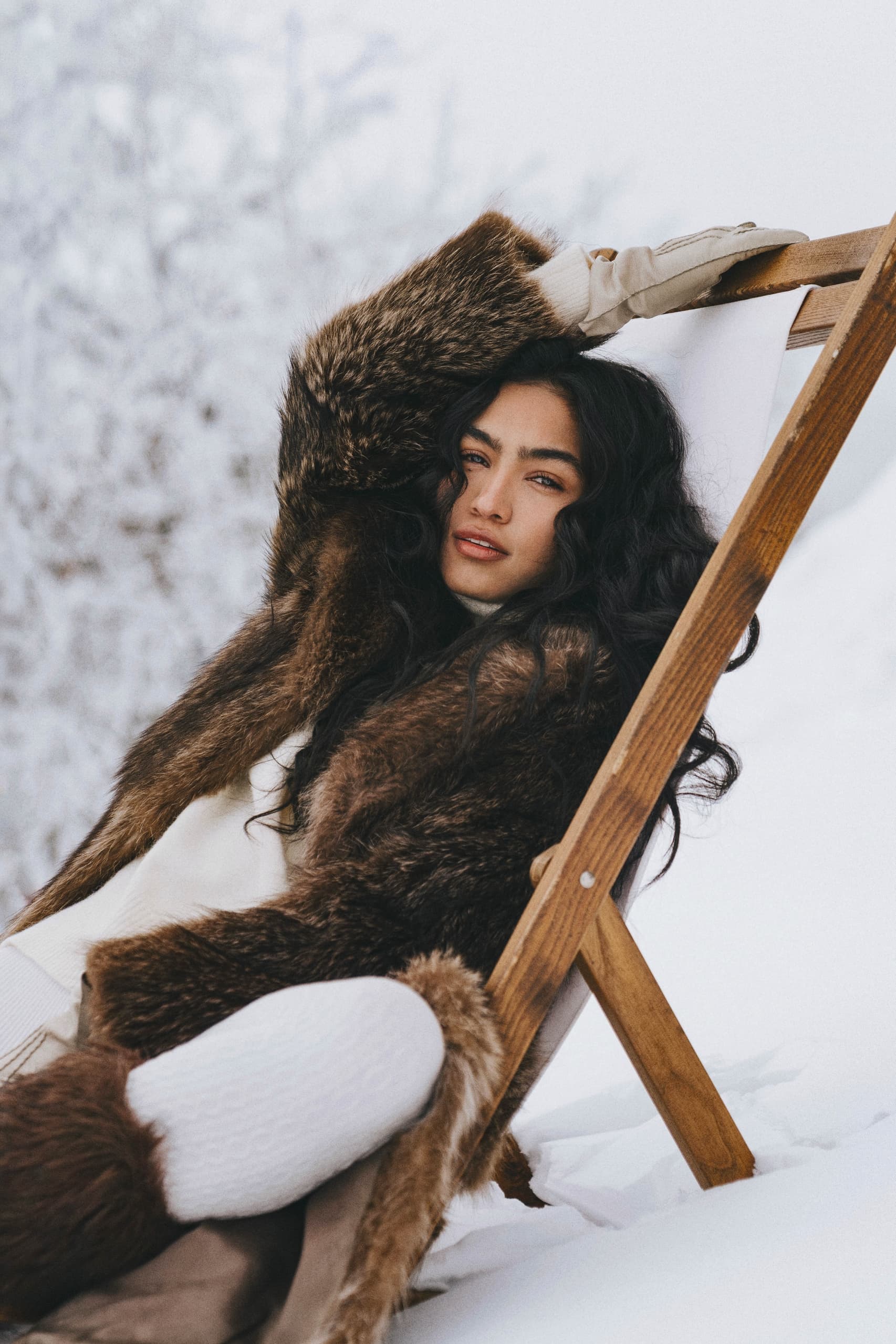 Woman in fur coat relaxing in snowy chair outdoors.