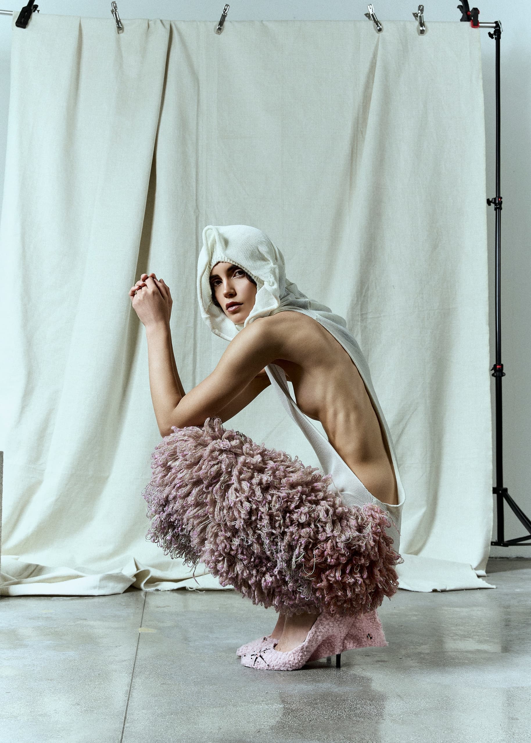 Fashion model in artistic pose with textured outfit and neutral background.