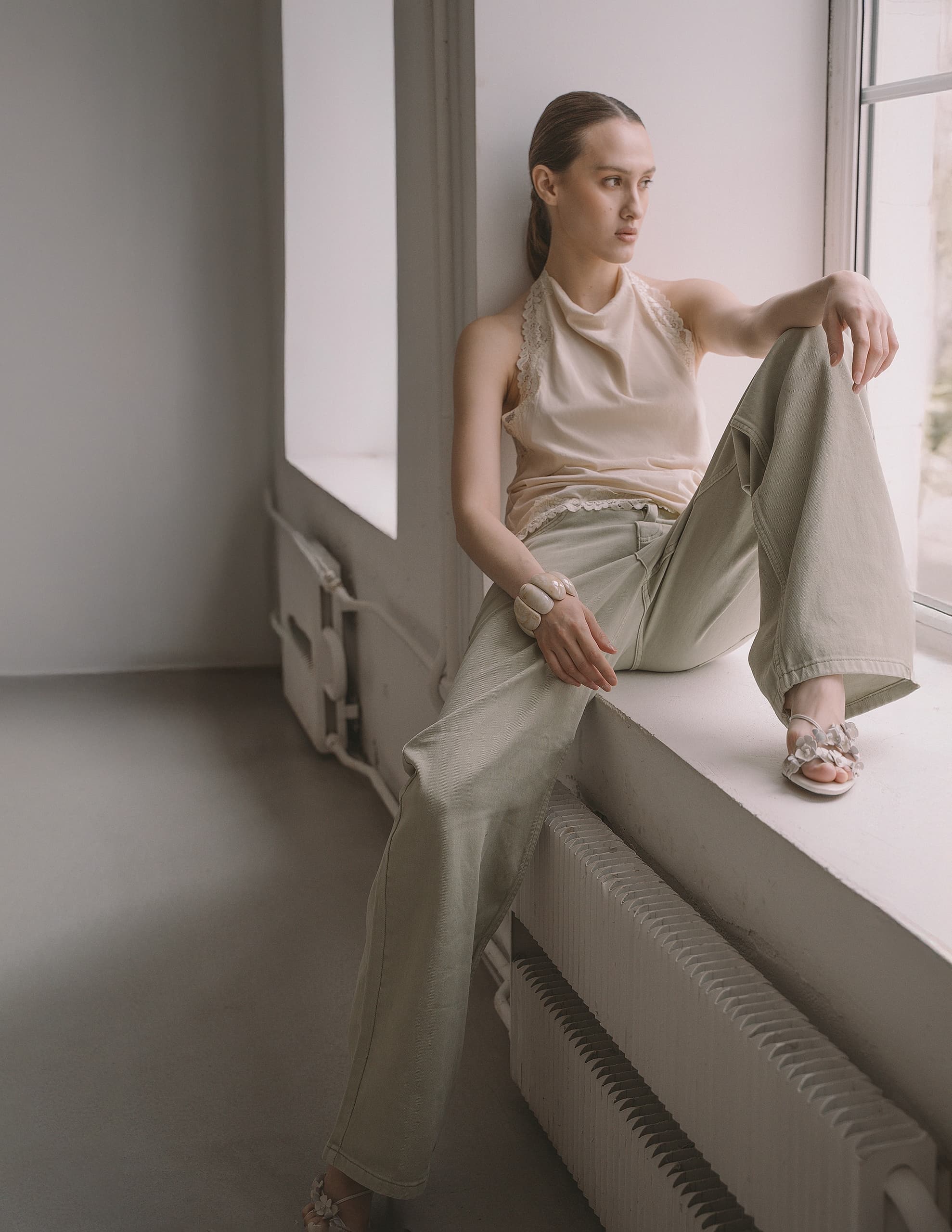 Woman in casual beige outfit sitting on windowsill, gazing outside.