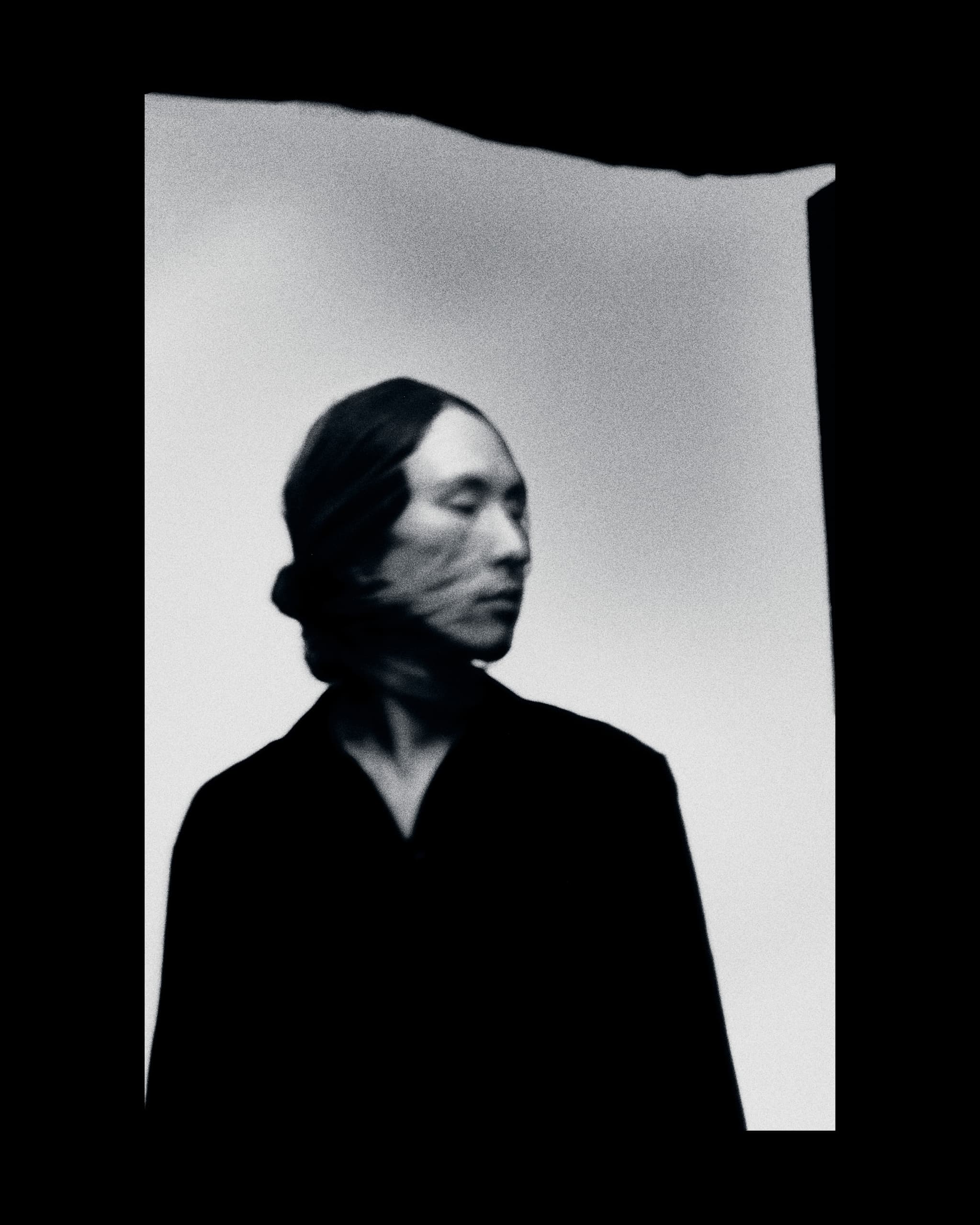 Blurry black and white portrait of a person with face partially wrapped in fabric.