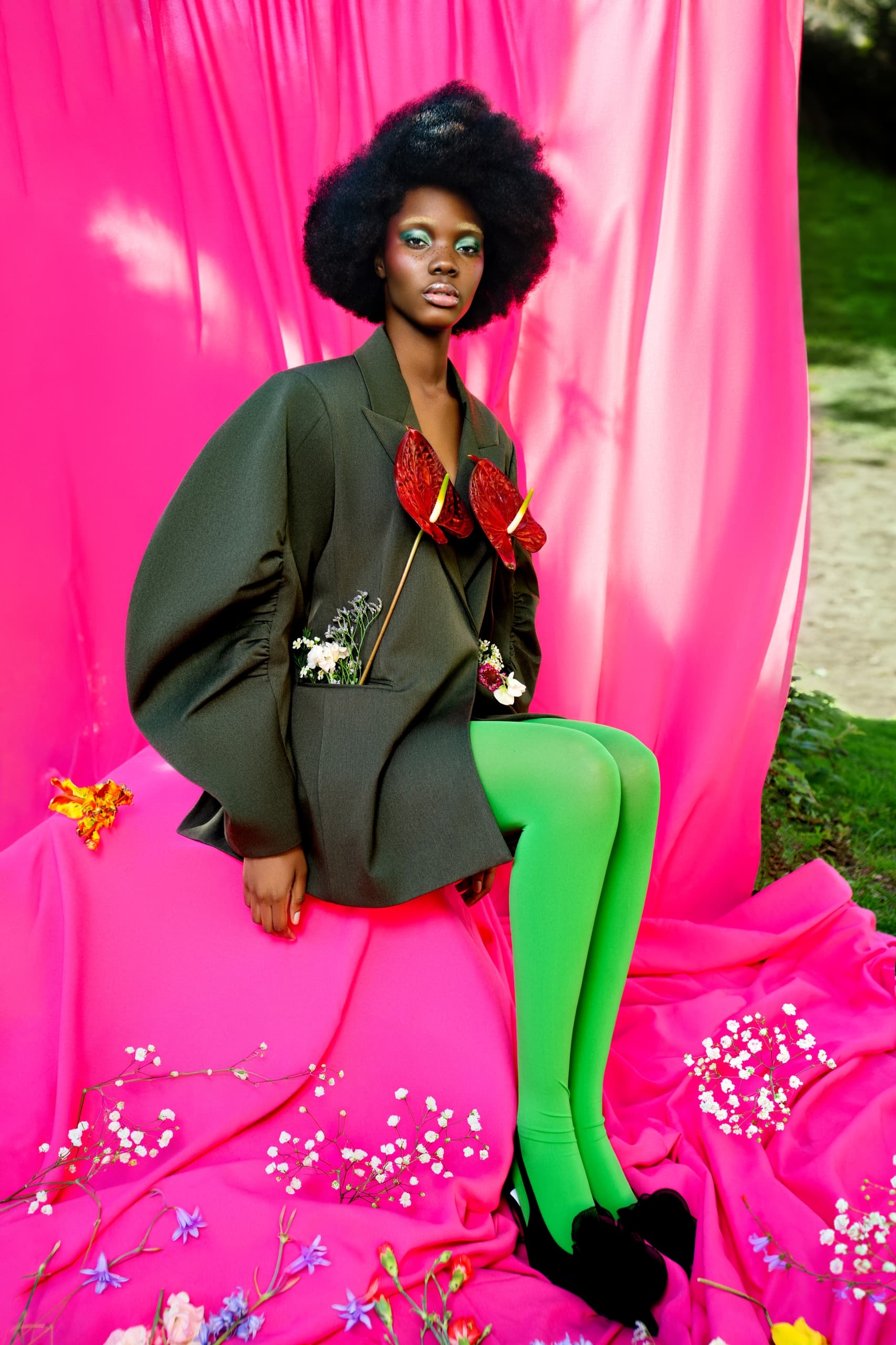 Fashionable model posing in a vibrant outfit with a pink and green backdrop.