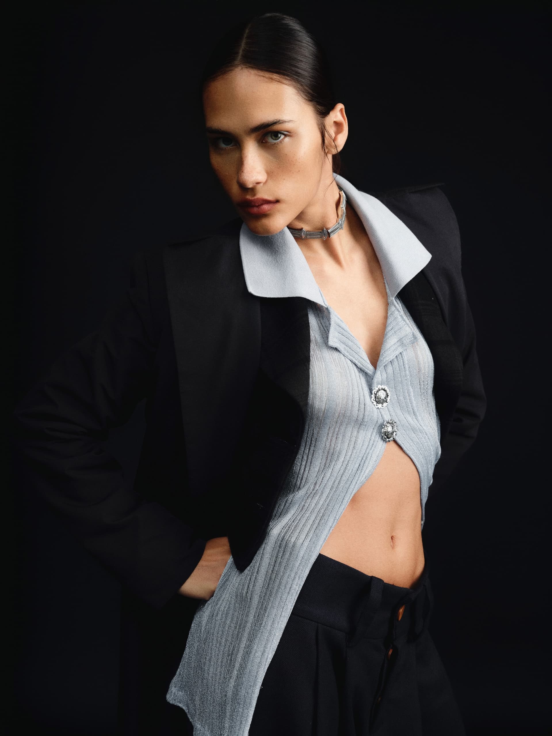 Fashion model posing in stylish black and grey outfit against a dark background.