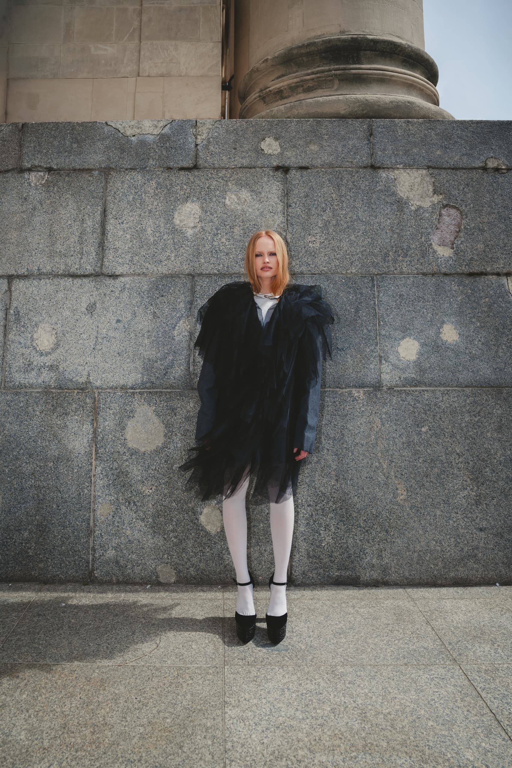 Woman in avant-garde black dress against stone wall. Fashion photography.