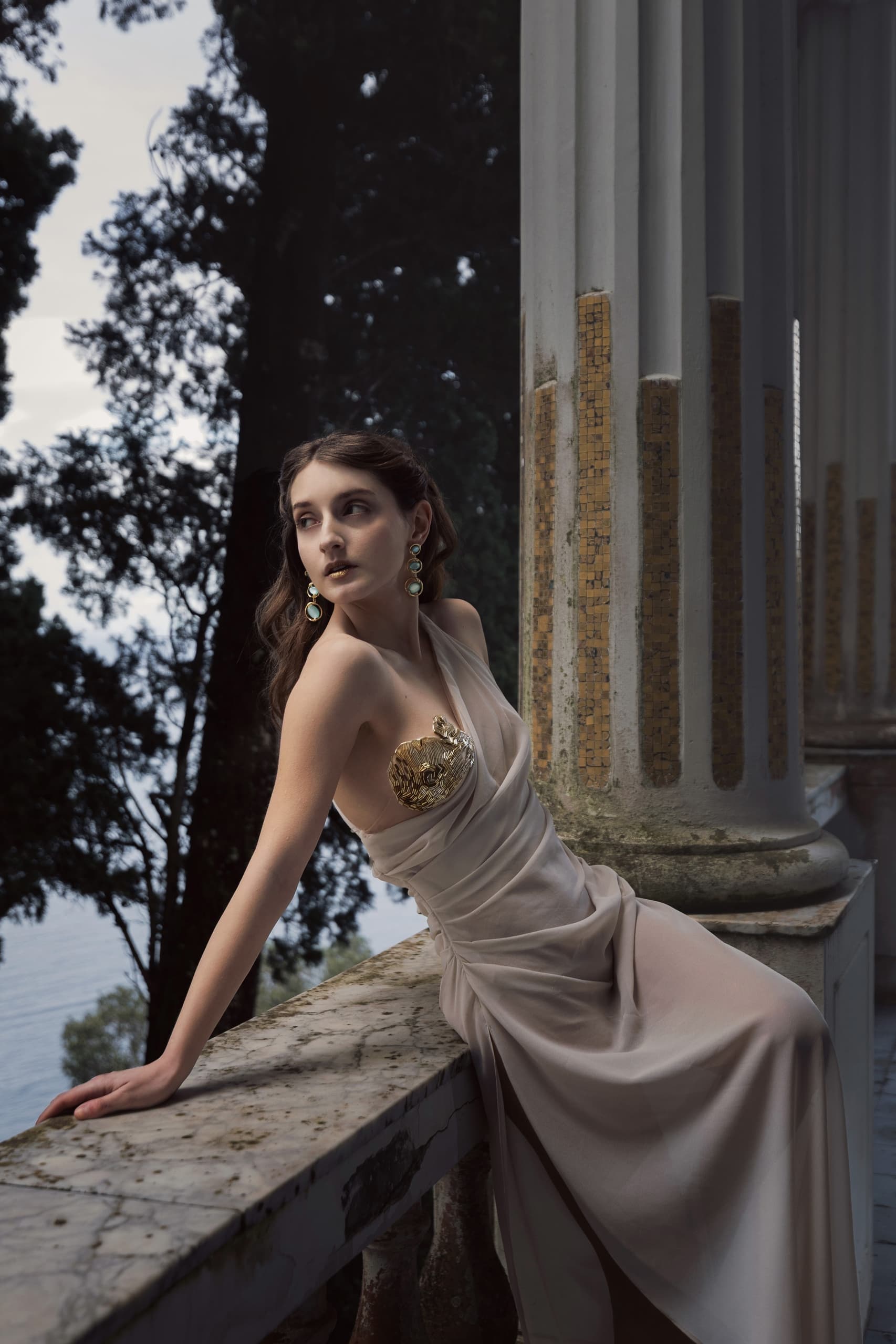 Elegant woman in gold-accented gown posing by decorative columns.