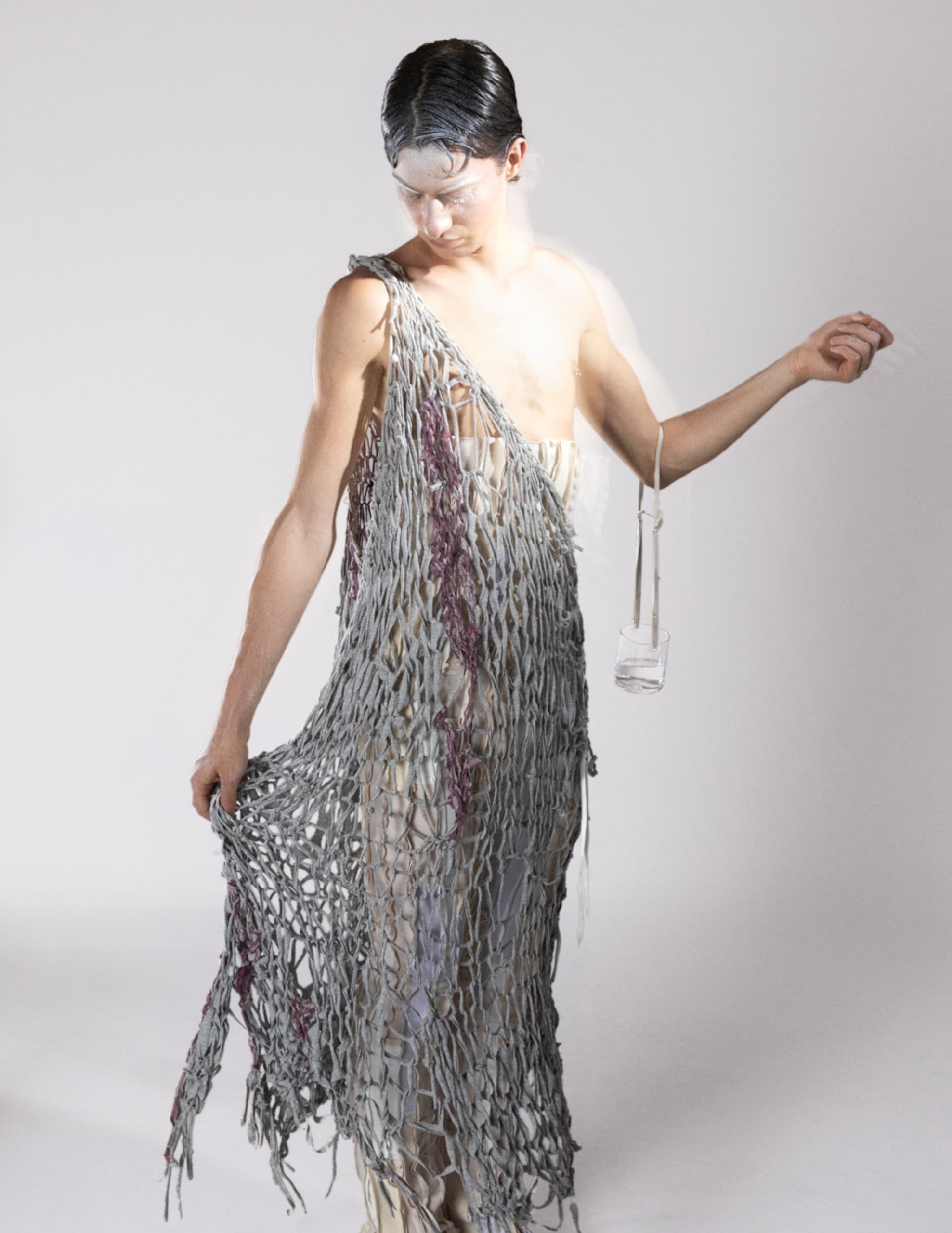 Person wearing gray textured net dress, looking down in a minimalist studio setting.