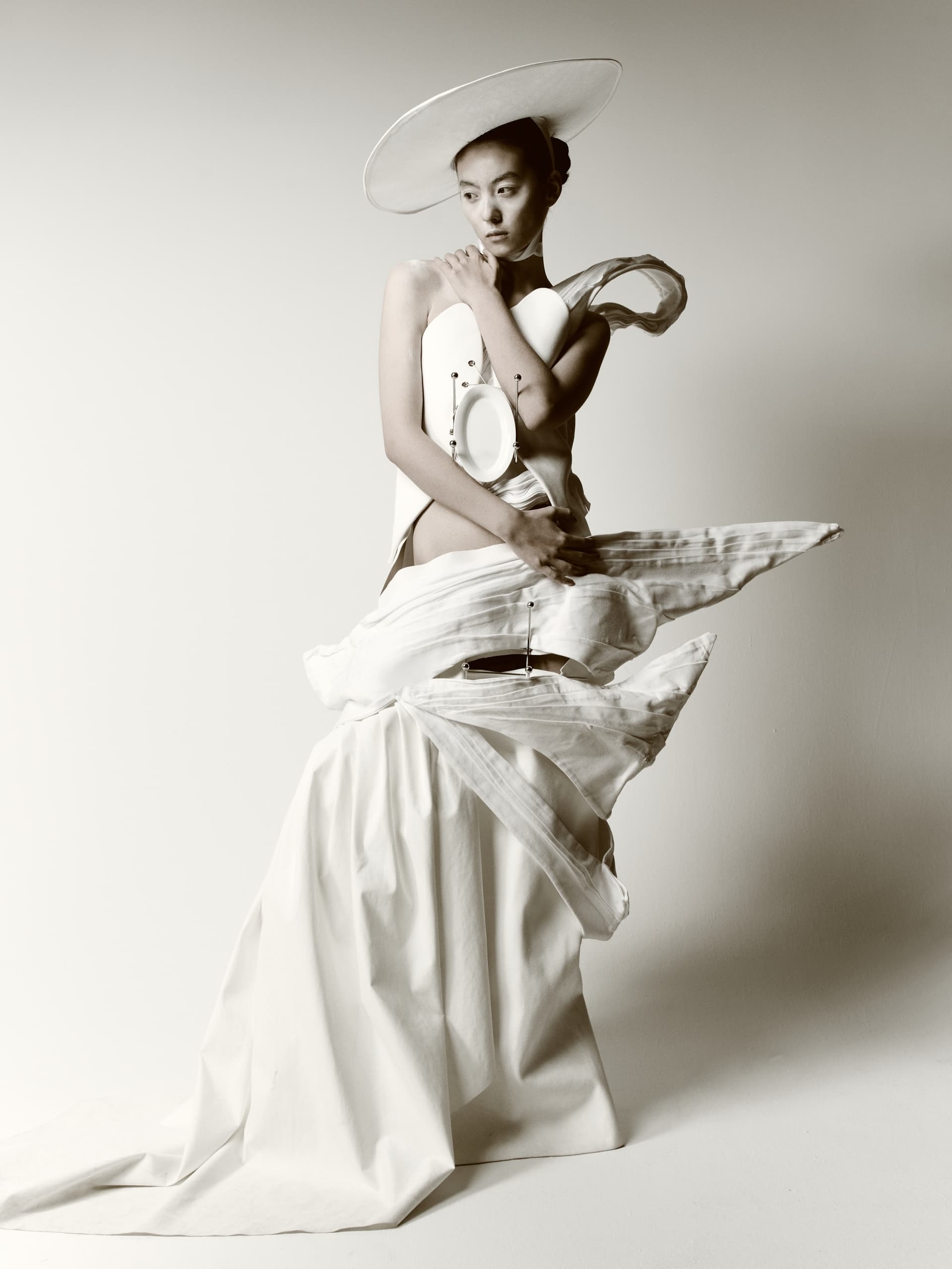 Avant-garde fashion model in a unique white dress and hat, striking a creative pose.