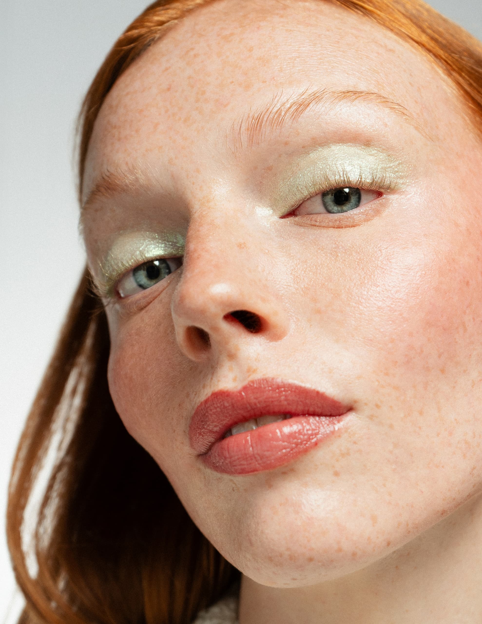 Close-up of woman with red hair, green eyeshadow, and natural lip makeup.