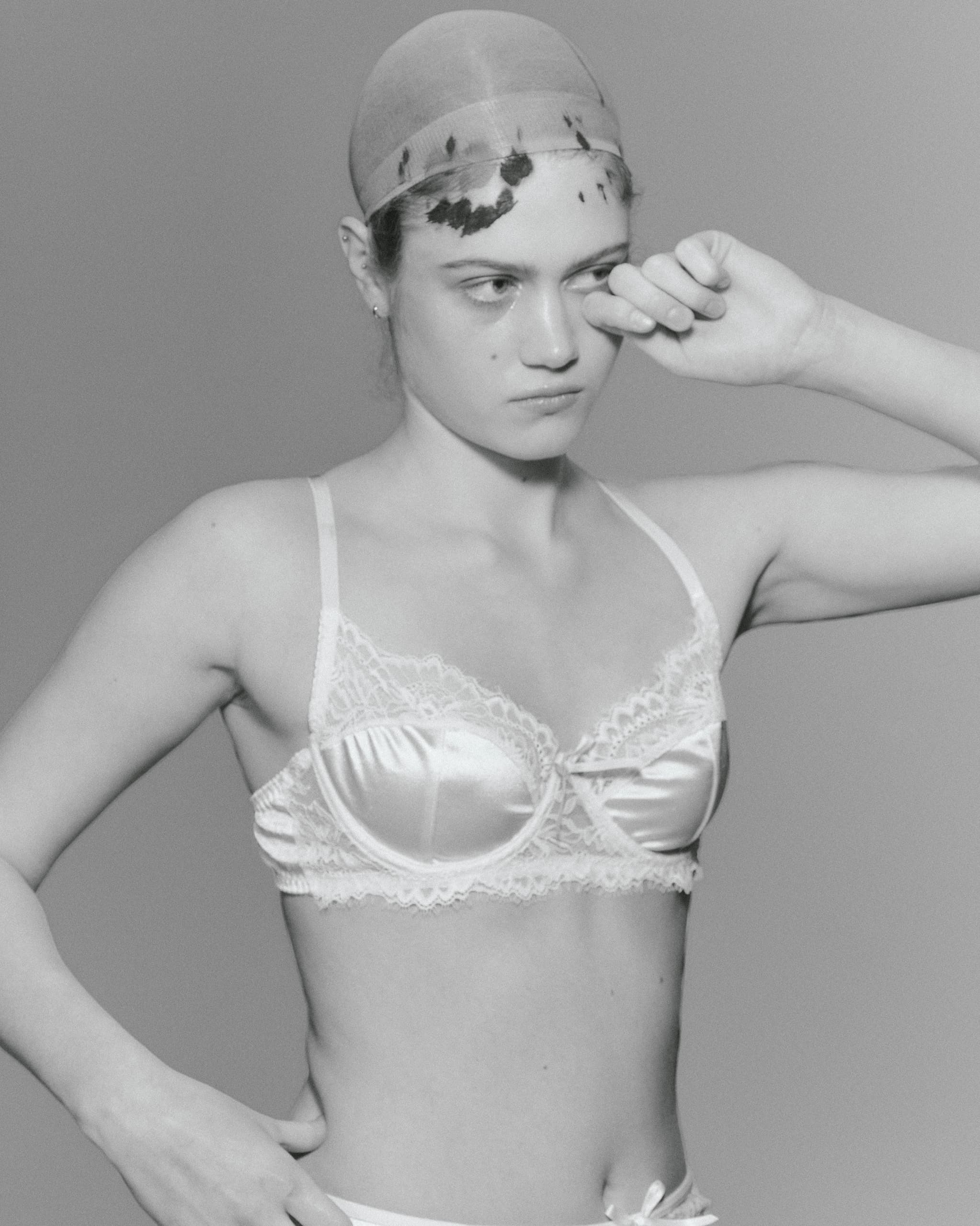 Black and white photo of model in lace lingerie against plain background.