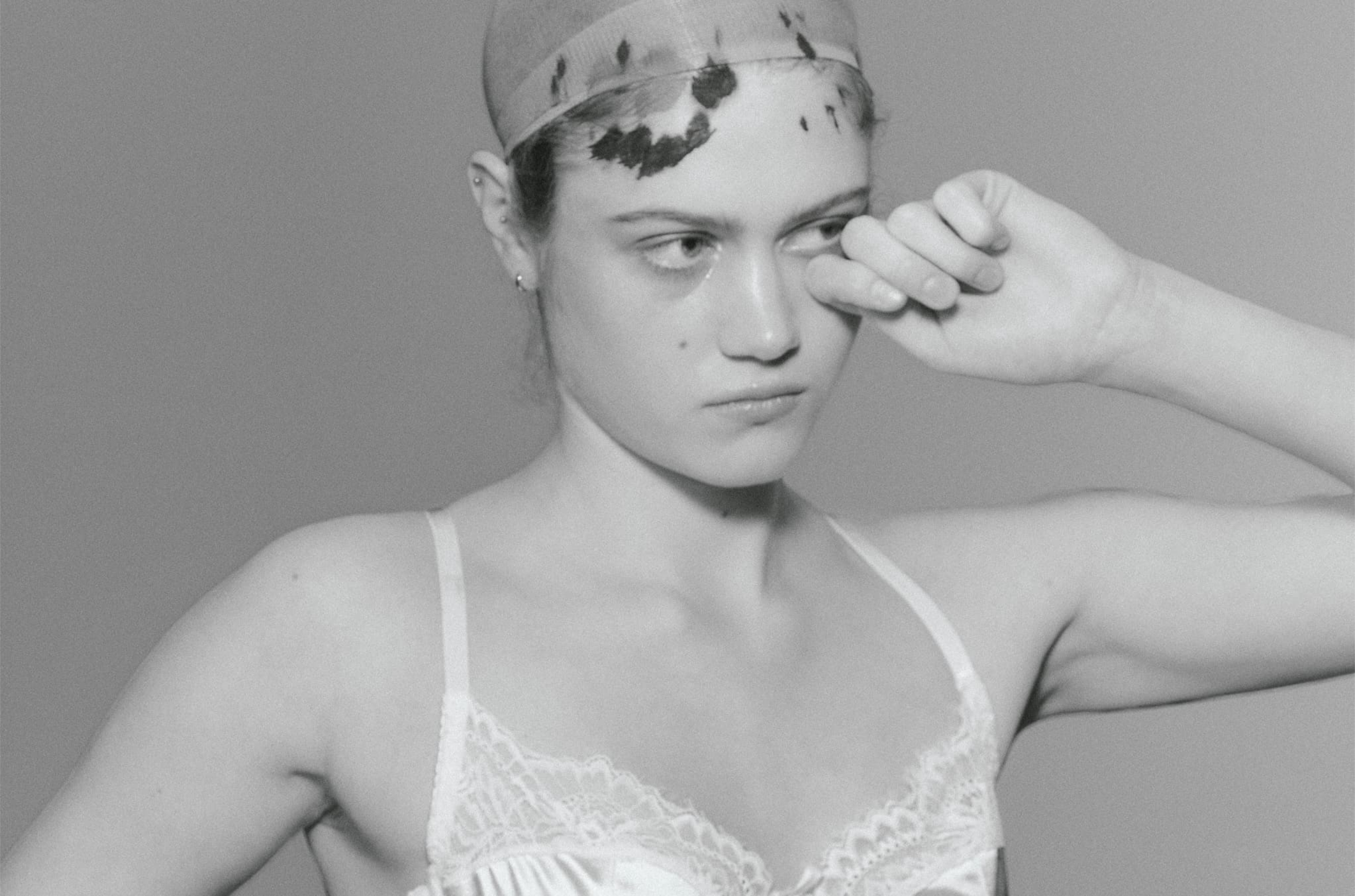 Black and white portrait of a woman adjusting a headpiece, wearing a lace top.