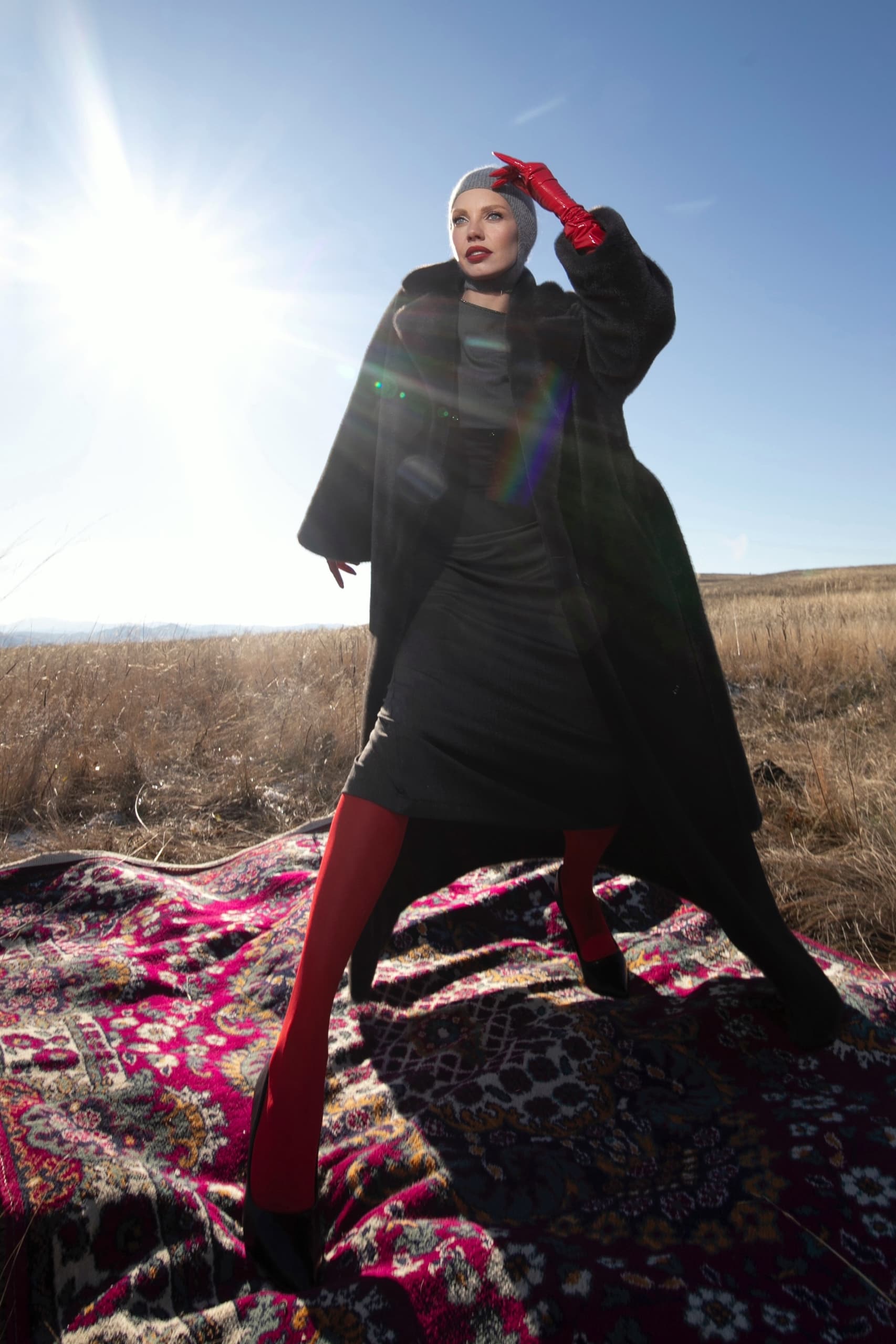 Fashionable woman poses outdoors in stylish coat, red gloves, and bright sunlight.