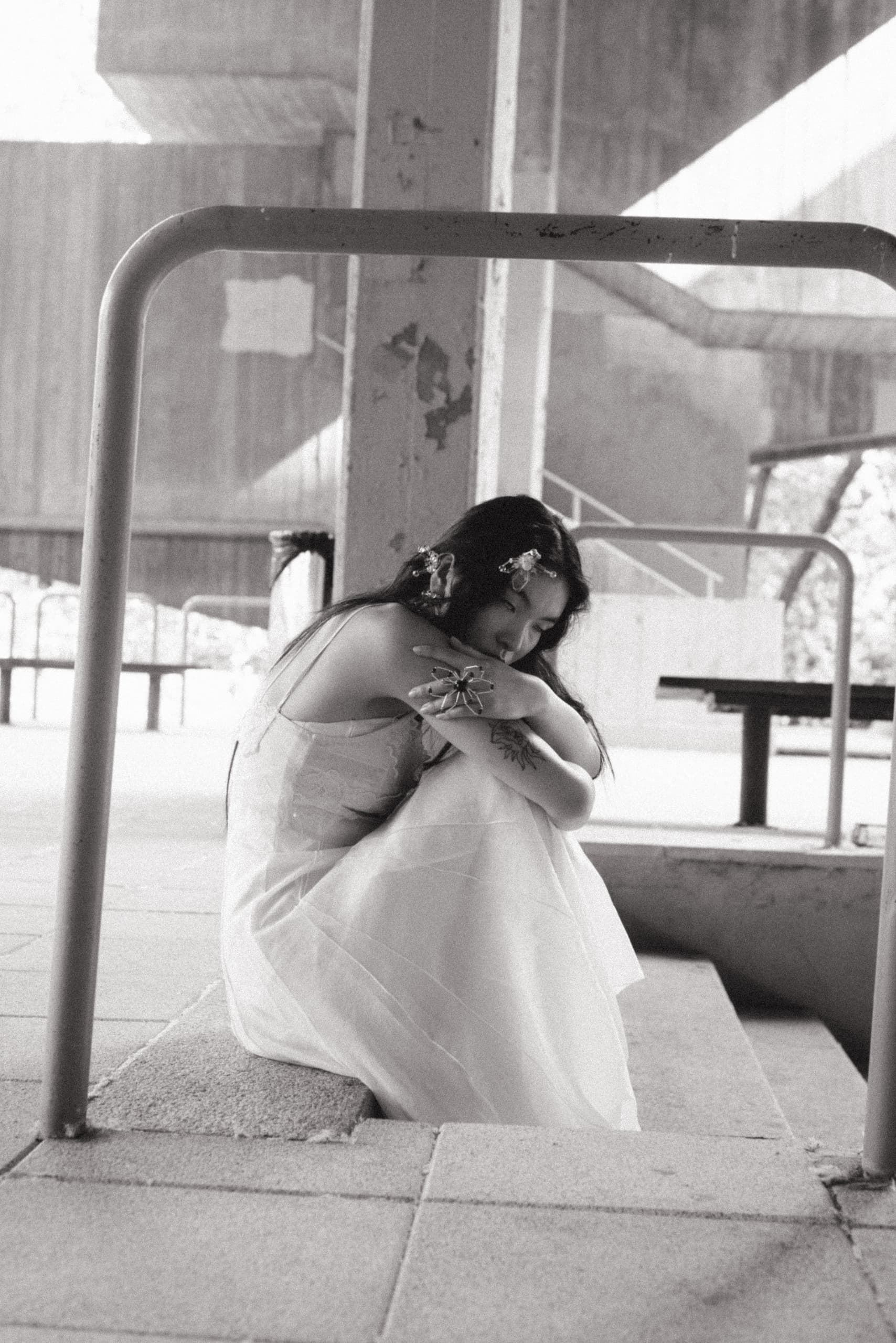 Woman in white dress sitting pensively in an industrial setting. Black and white photo.