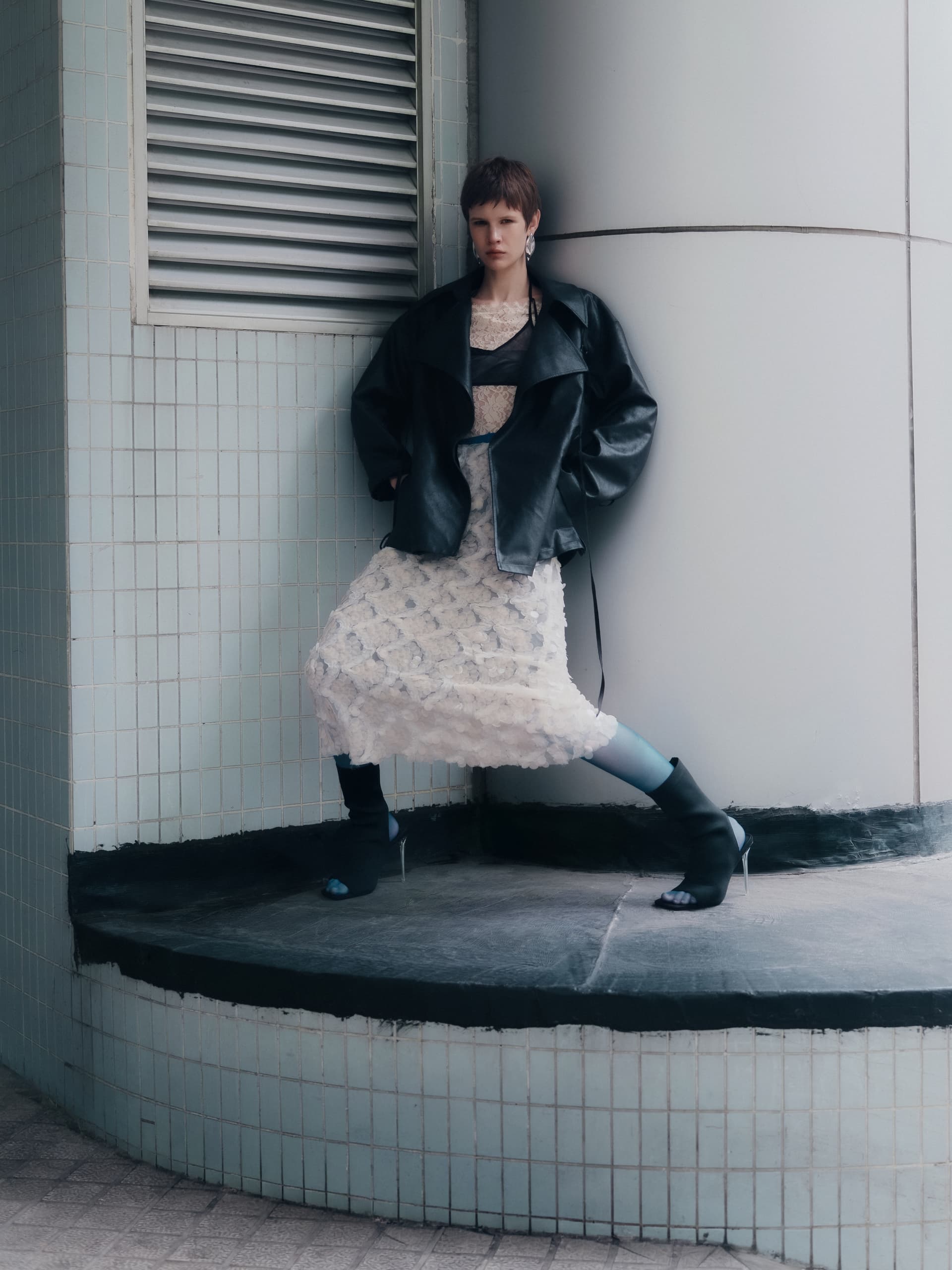 Fashionable model in modern outfit with layered textures and sleek black jacket.