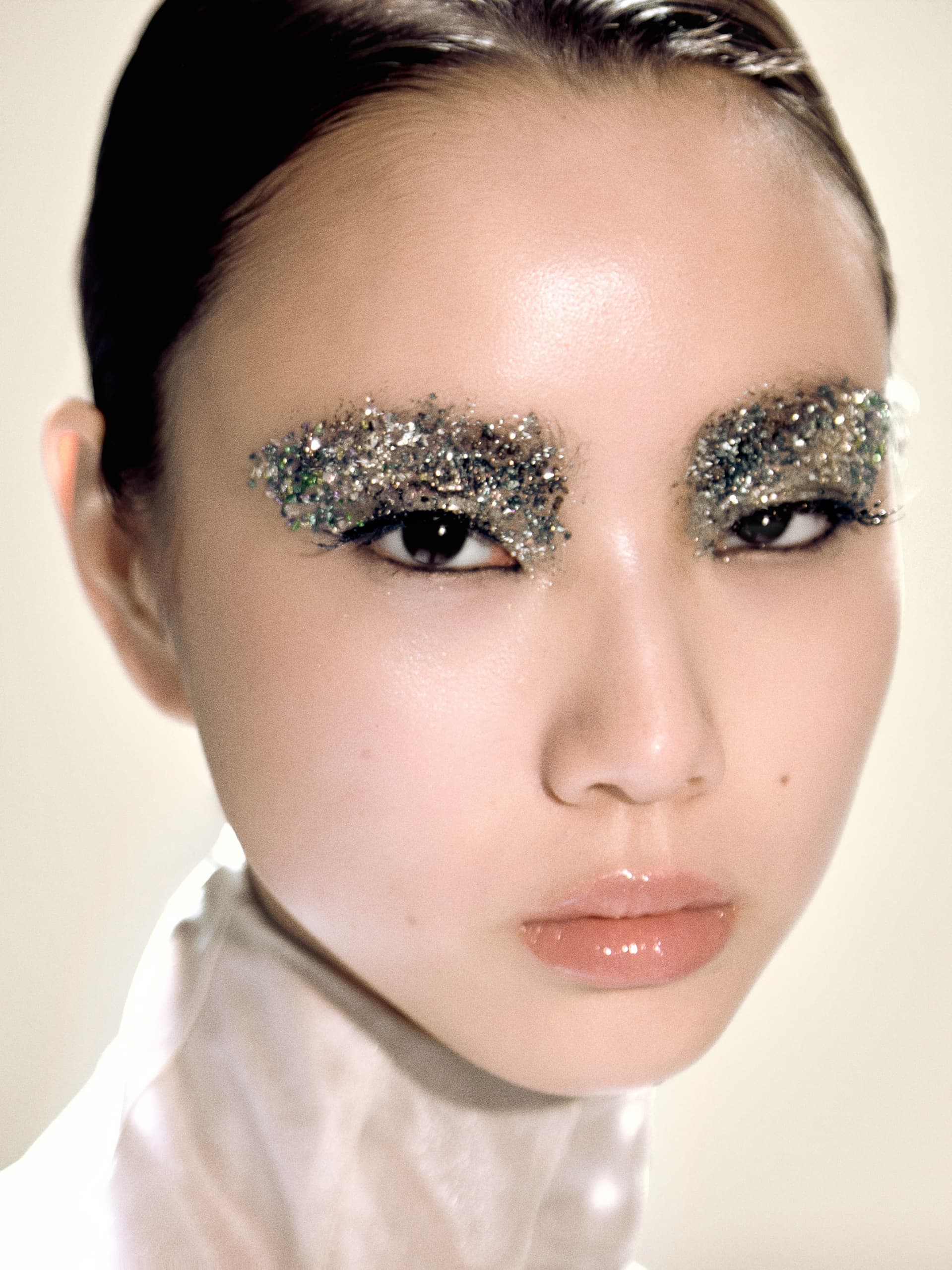 Model with glitter eyebrows and glossy lips in a close-up portrait.