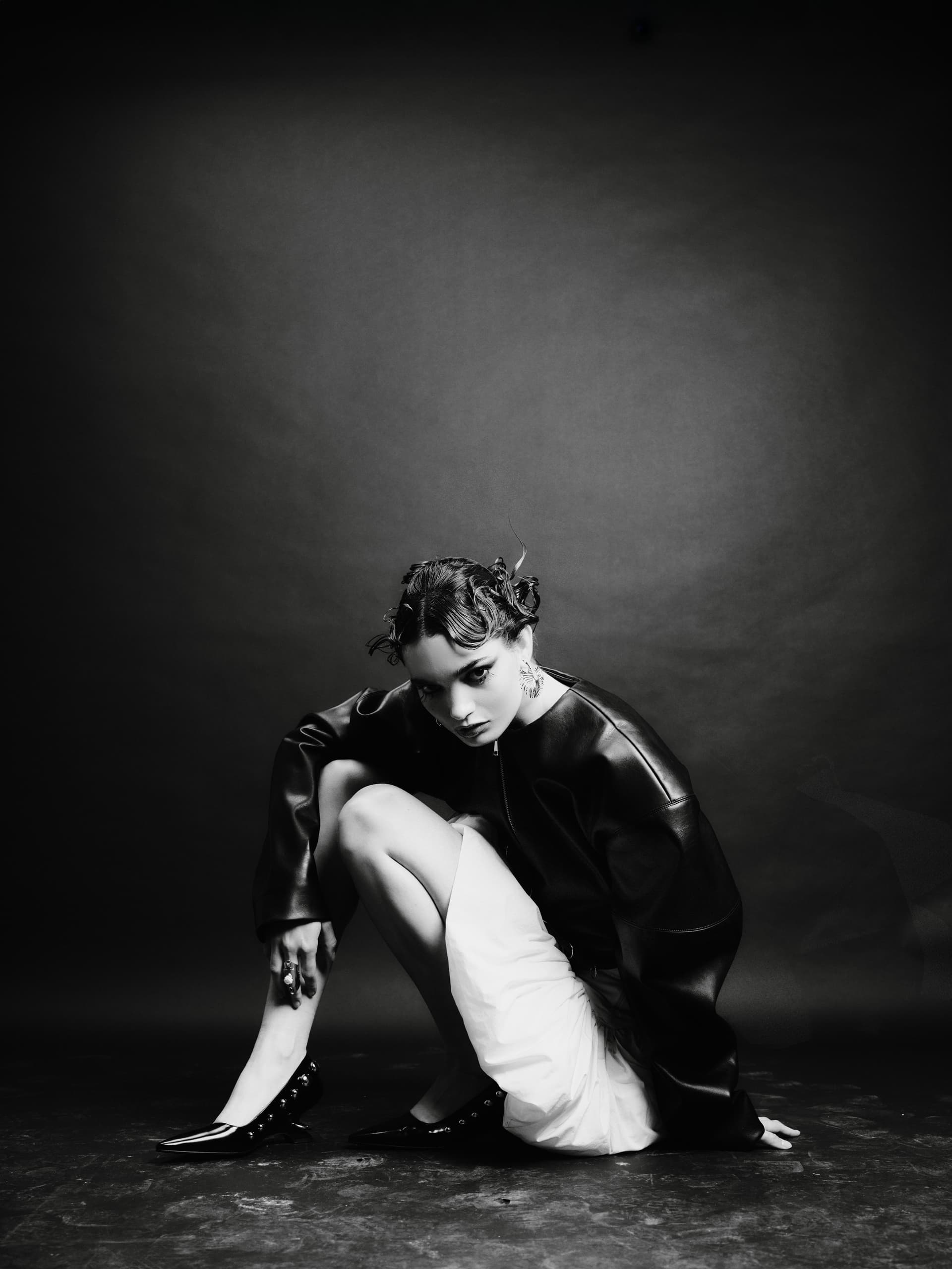 Black and white fashion portrait of a woman in edgy attire, crouching gracefully.