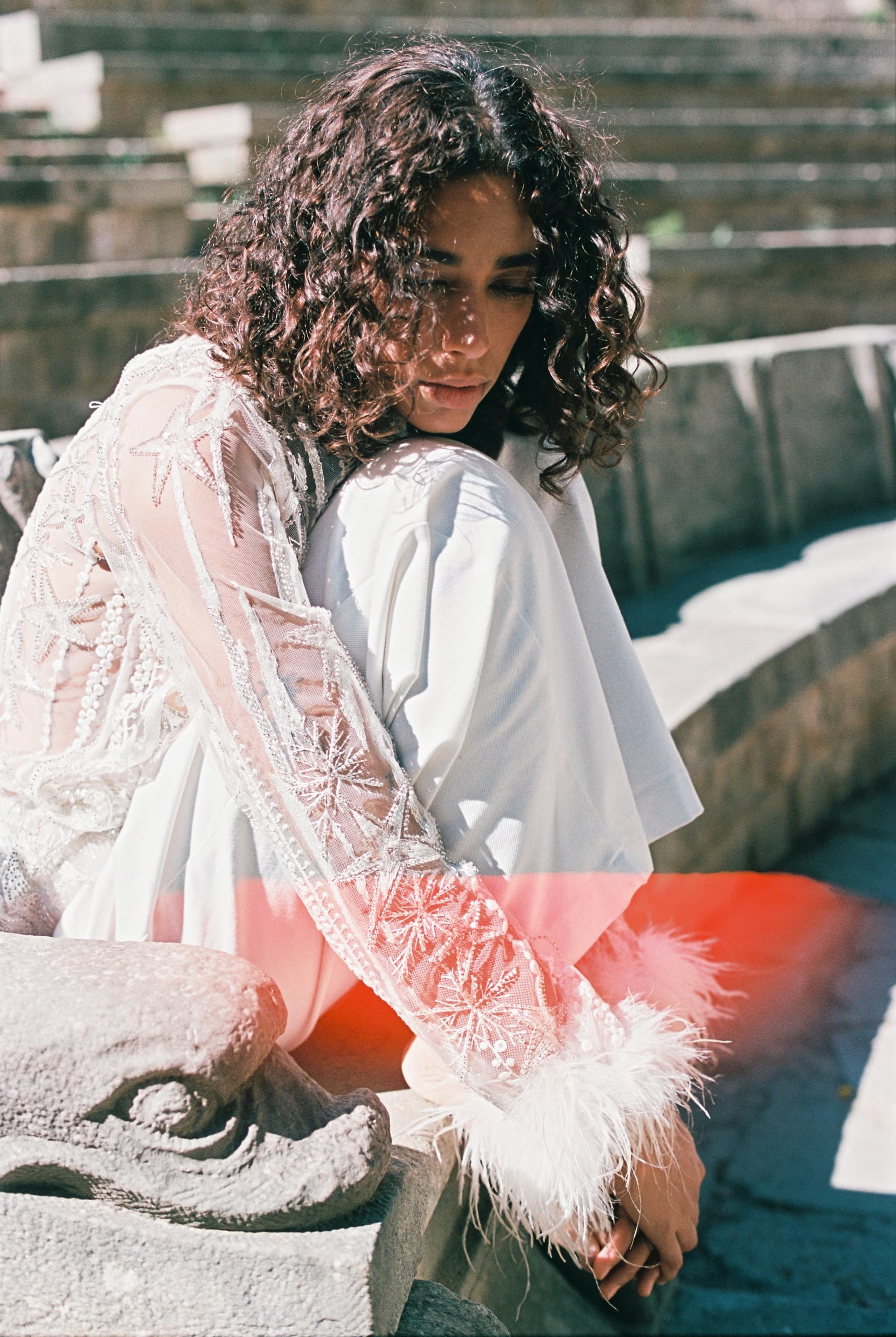 Woman in elegant lace attire seated on stone steps outdoors.