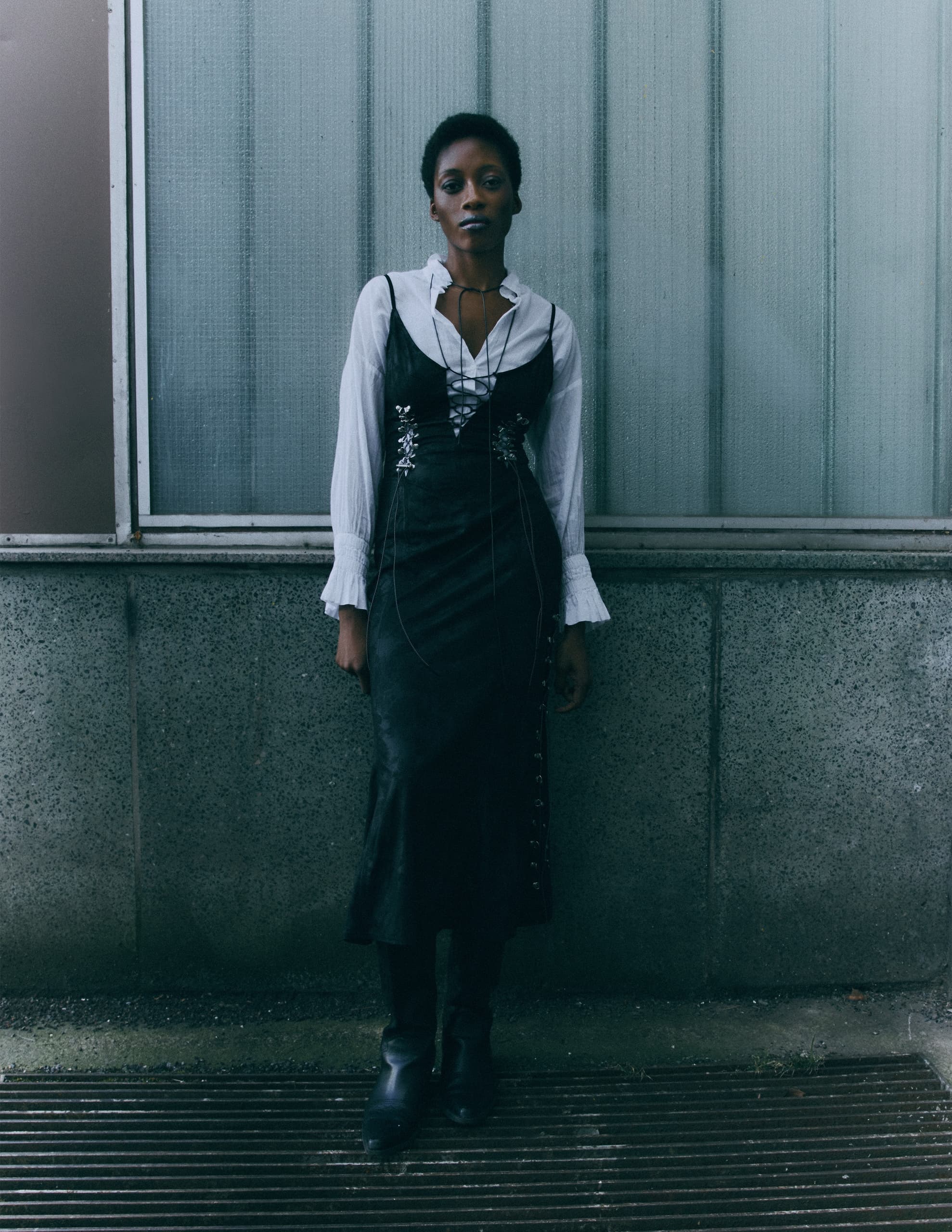 Fashionable person in a layered dress standing against a textured glass wall.