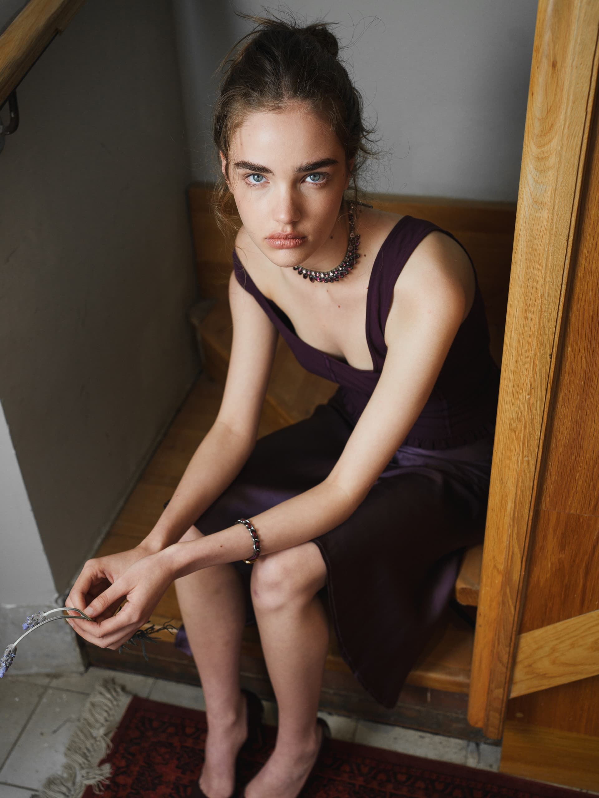 Woman in elegant purple evening dress sitting on wooden stairs, holding lavender.