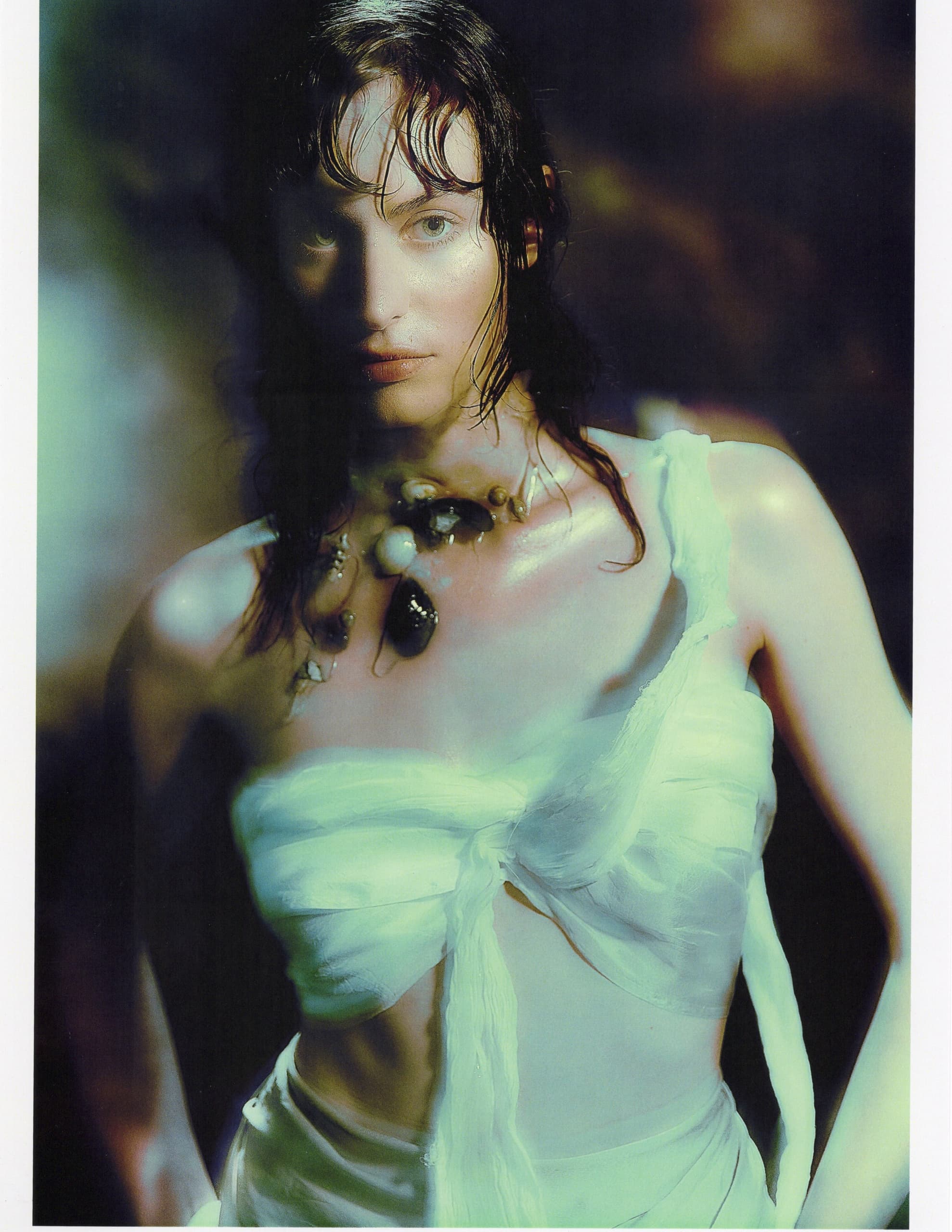 Model in ethereal lighting wearing a white top and shell necklace.
