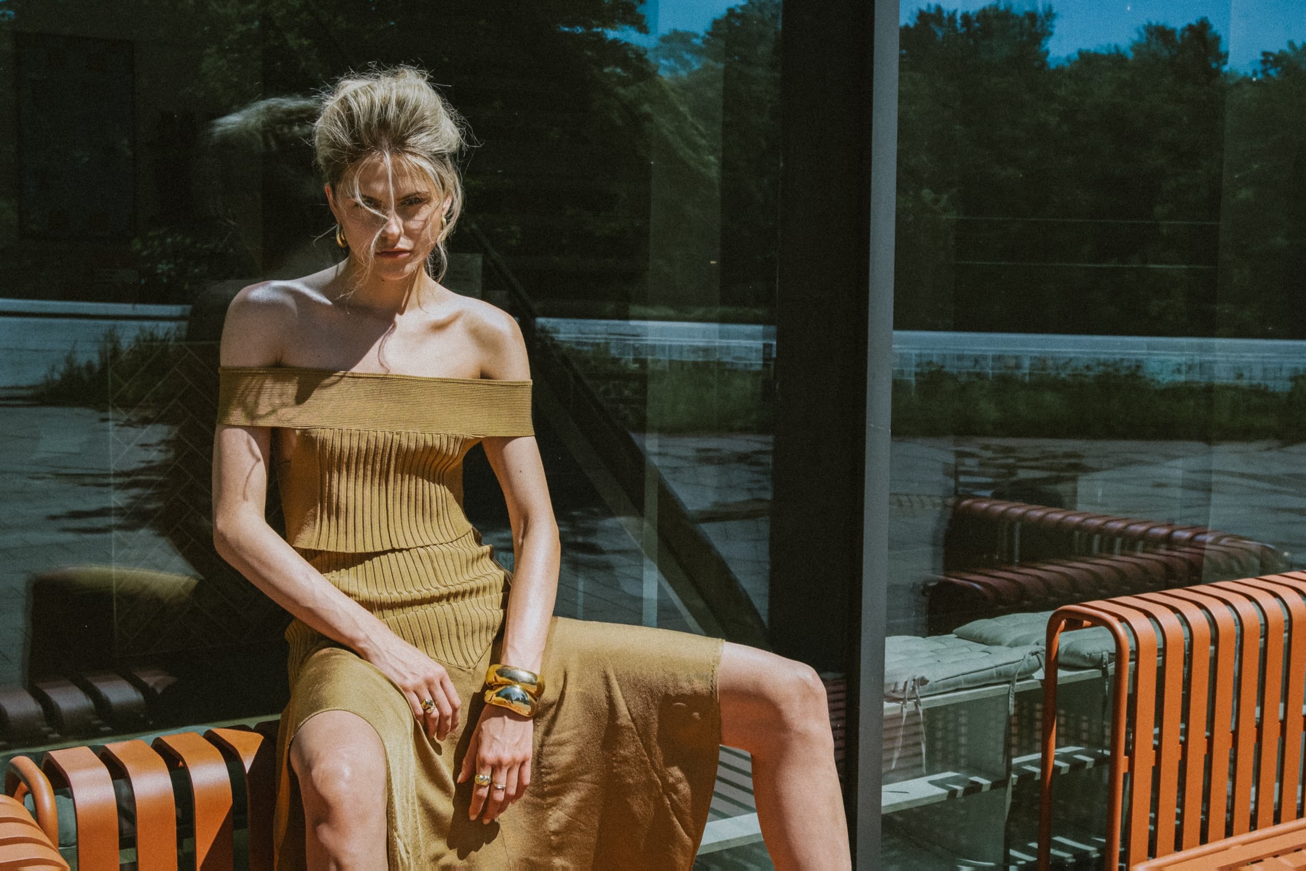 Woman in a stylish off-shoulder dress sitting outdoors on a sunny day.