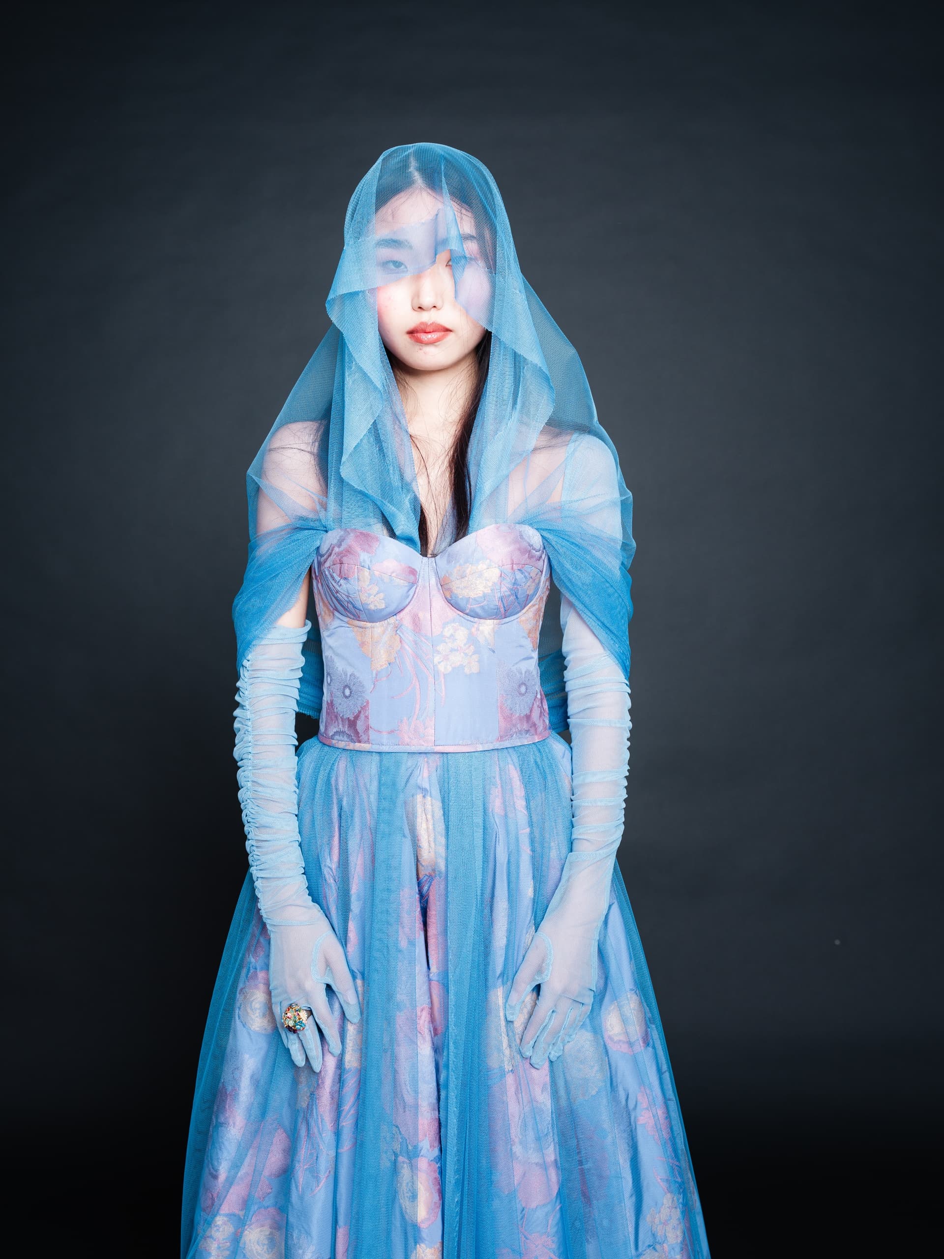 Woman in elegant blue veil and gown, posing against dark background.