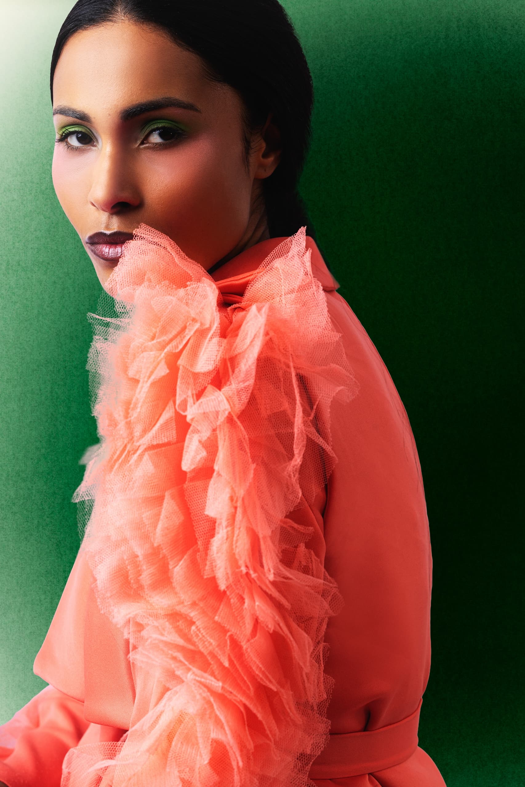 Woman in orange ruffled outfit with green background, elegant and stylish portrait.