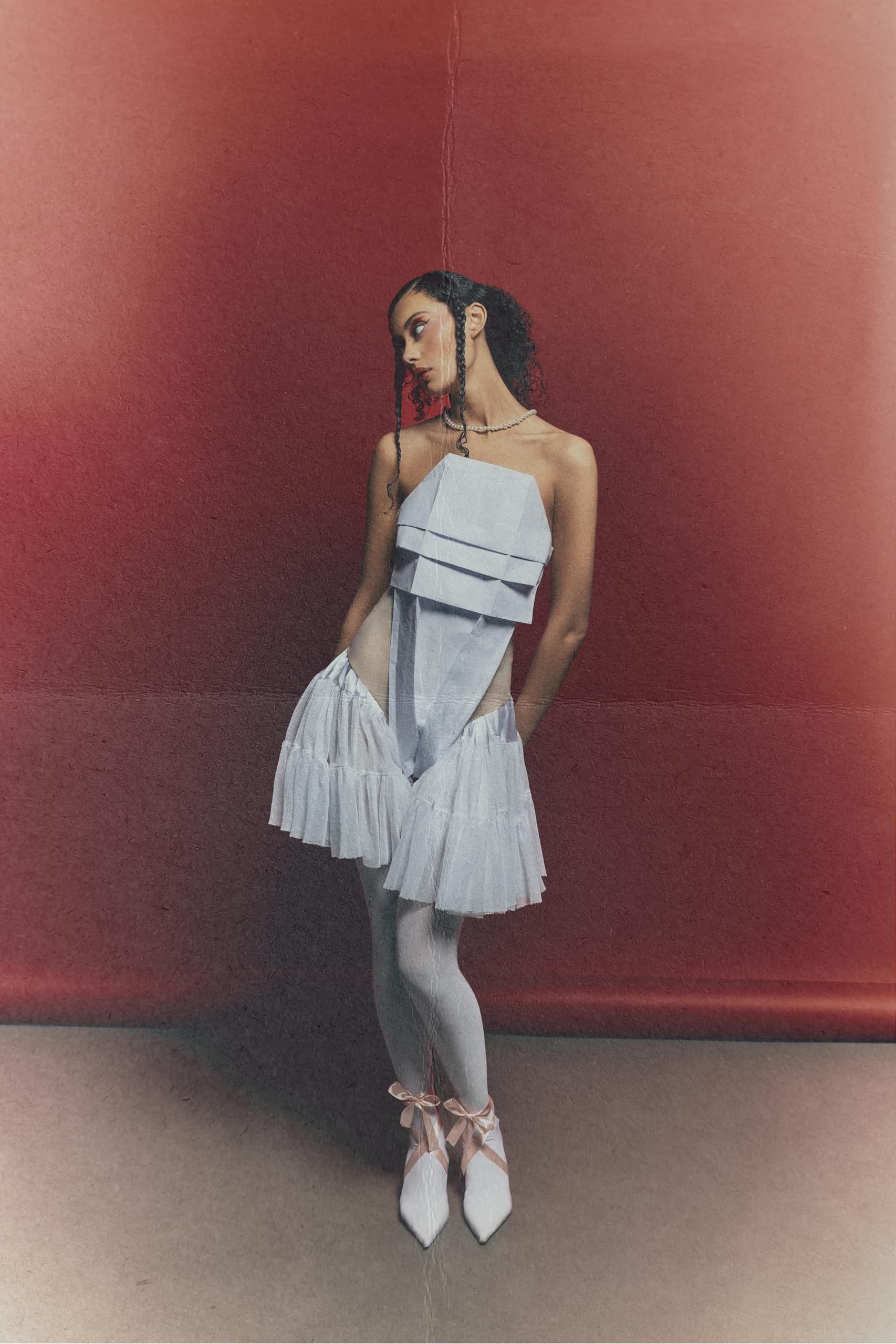 Woman in layered white dress against textured red background. Fashion editorial style.