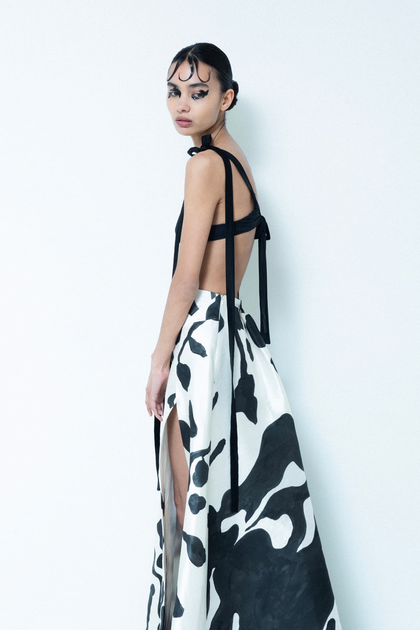 Model in a black top and patterned skirt, striking a stylish pose against white backdrop.