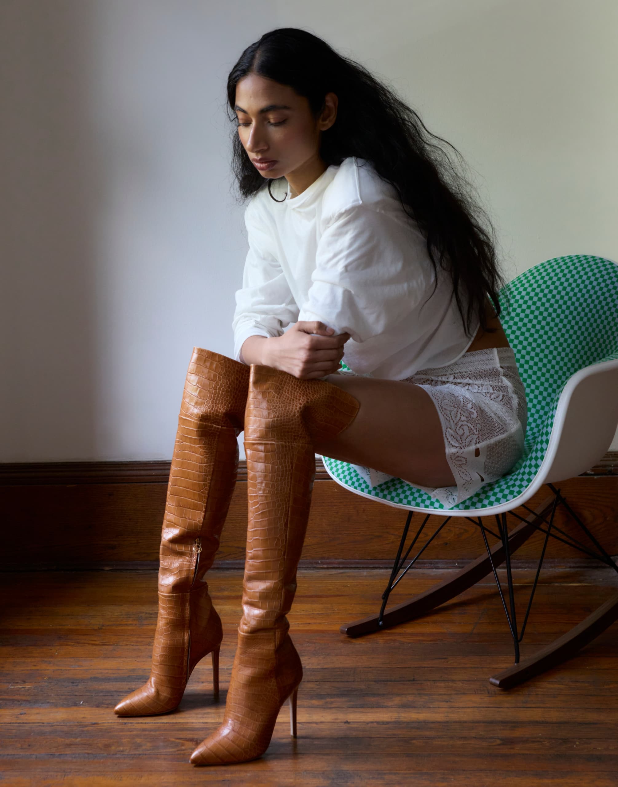 Woman in white shirt and brown boots seated on chair, looking down pensively.