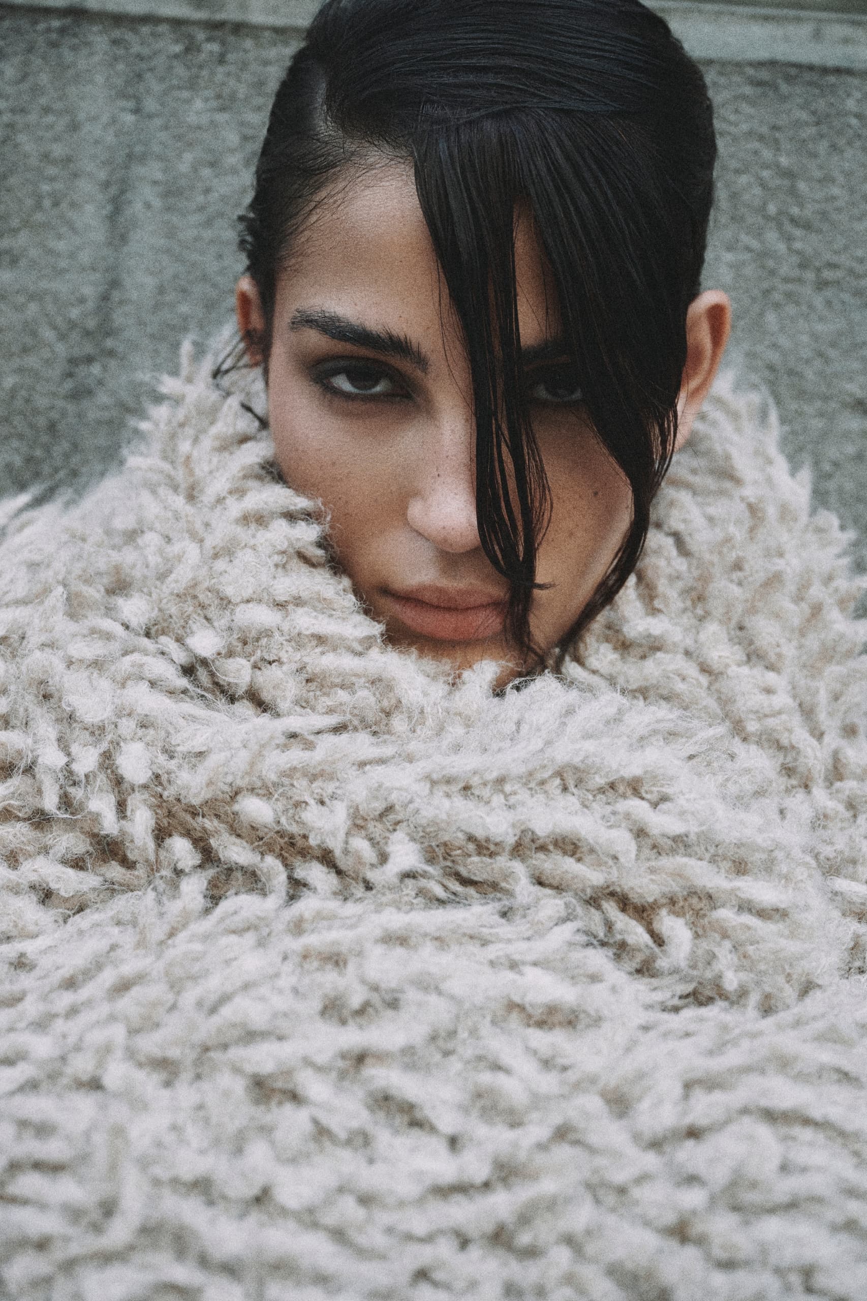 Woman wrapped in a cozy textured coat with intense gaze.