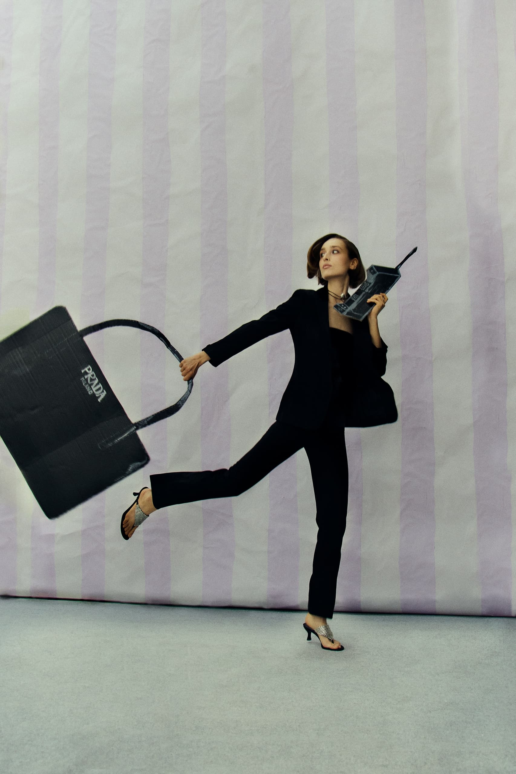 Fashionable woman with large Prada bag and vintage phone in chic black suit.