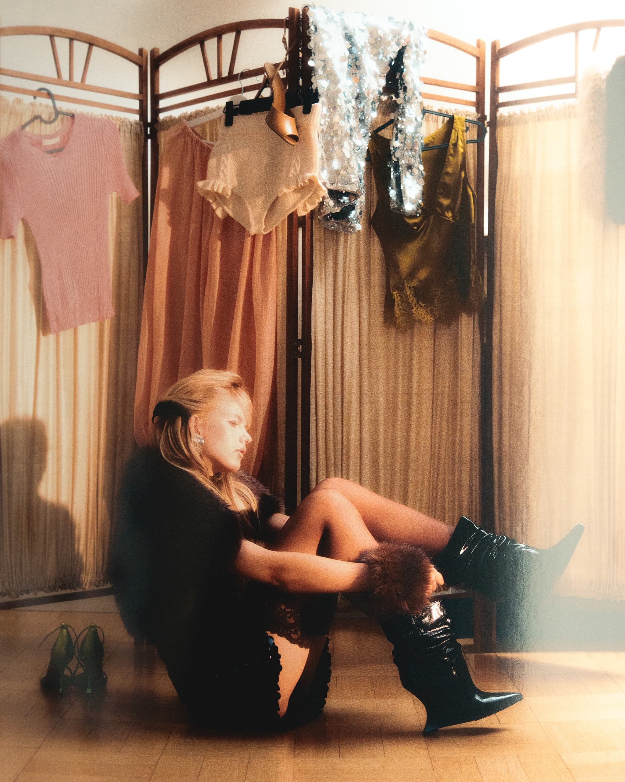 Woman sitting on floor in fashion apparel with clothing rack backdrop.