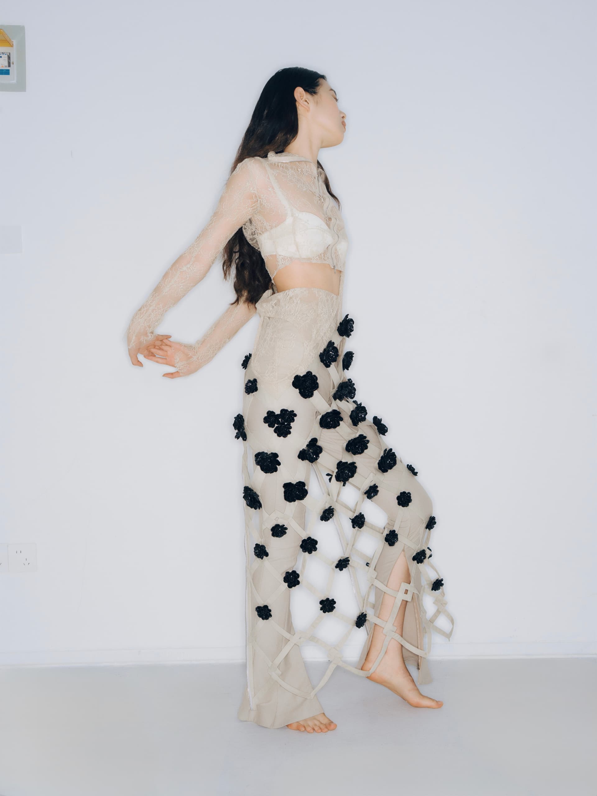 Fashion model in lace outfit with black floral accents against a white background.