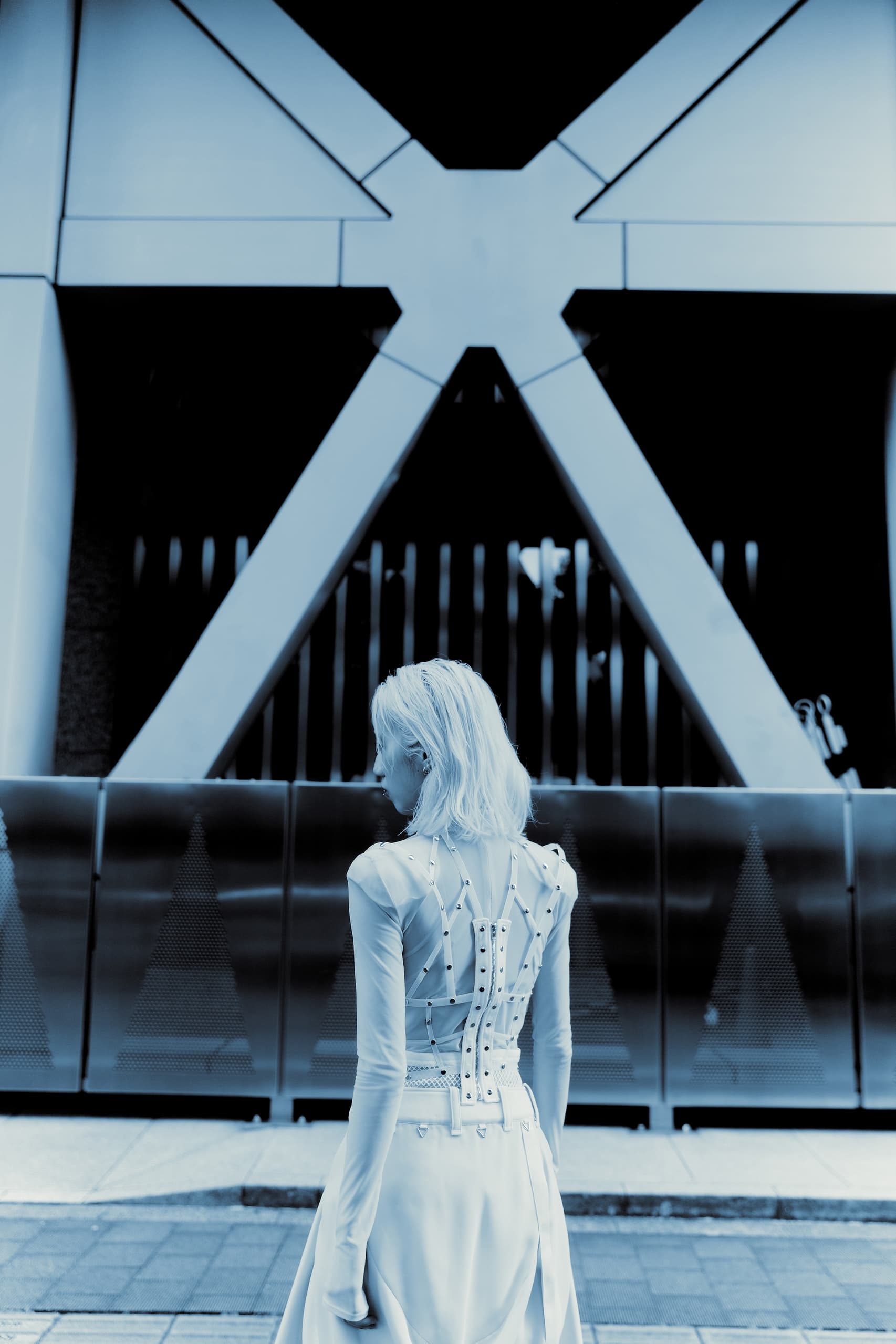Fashionable woman in futuristic dress stands before modern architecture.