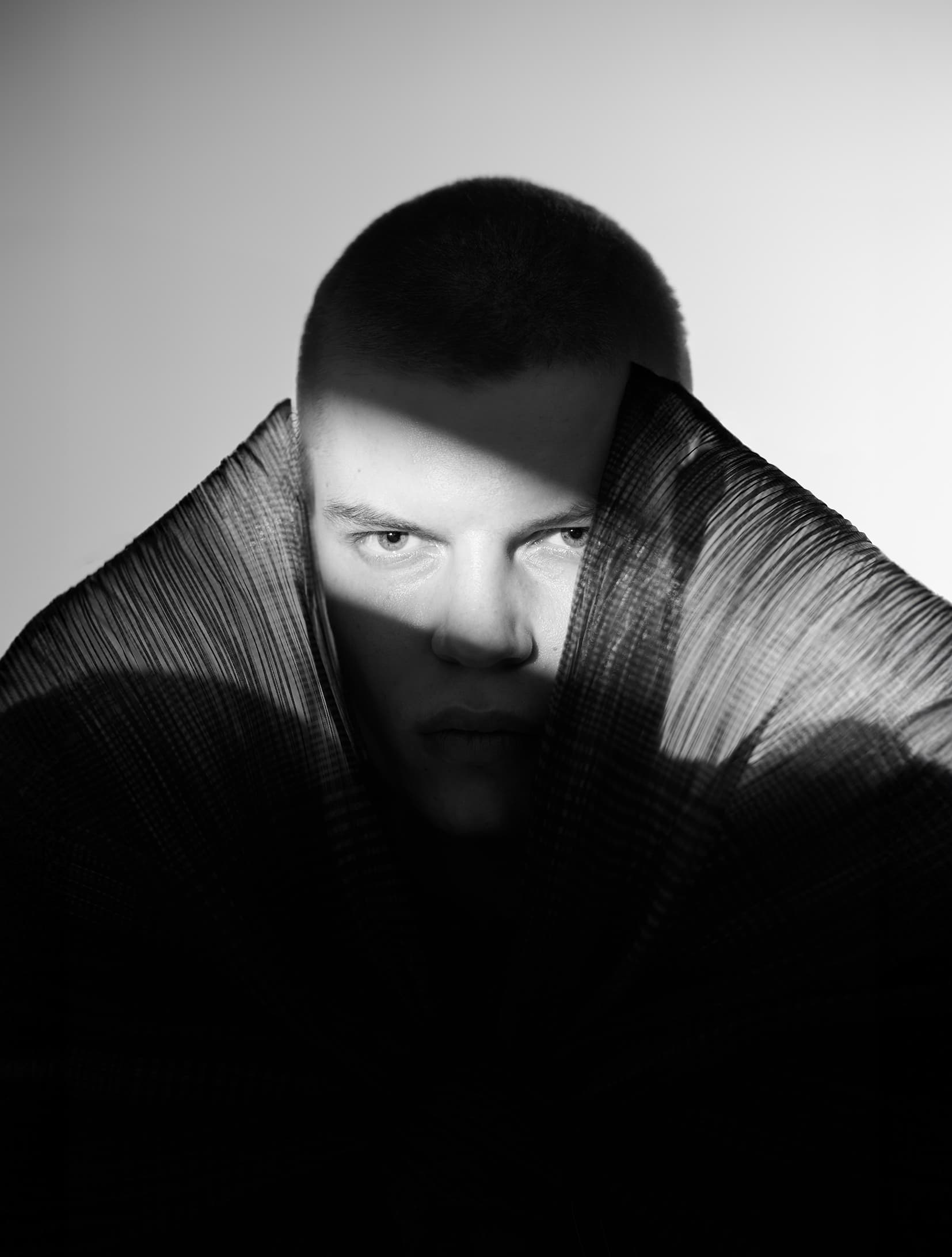 Dramatic black and white portrait with shadowed face and textured fabric.