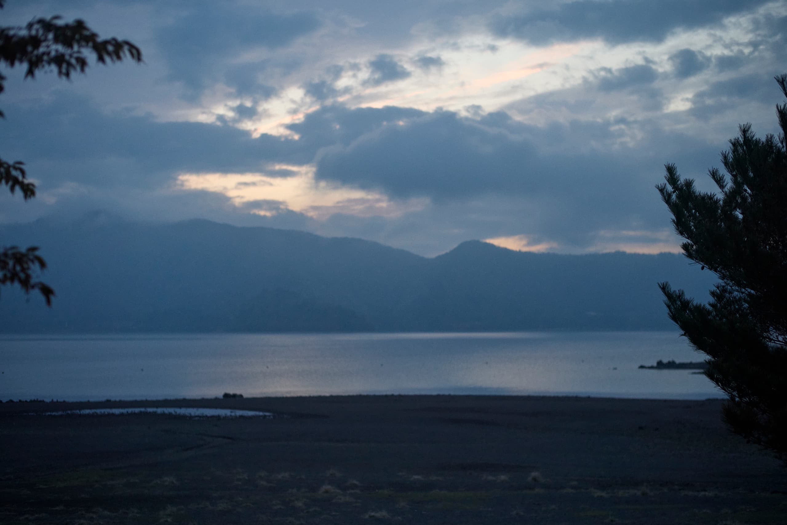 Serene lake view at dusk with silhouetted mountains and cloudy sky.