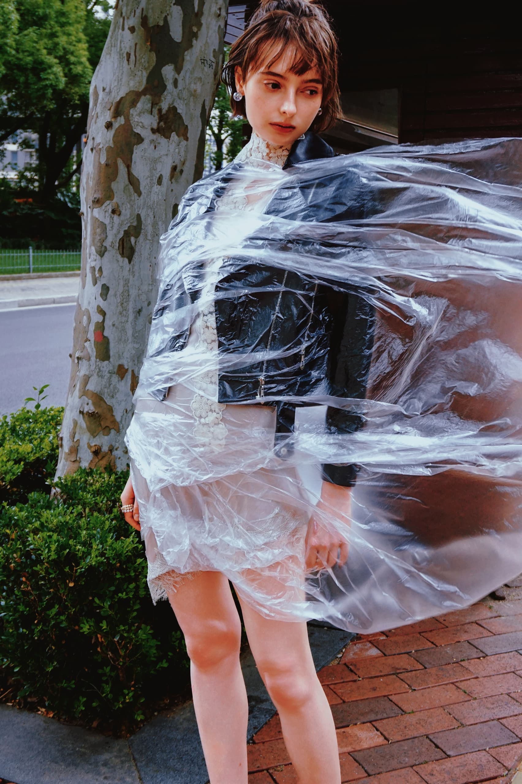 Fashion model wrapped in flowing clear plastic outdoors.