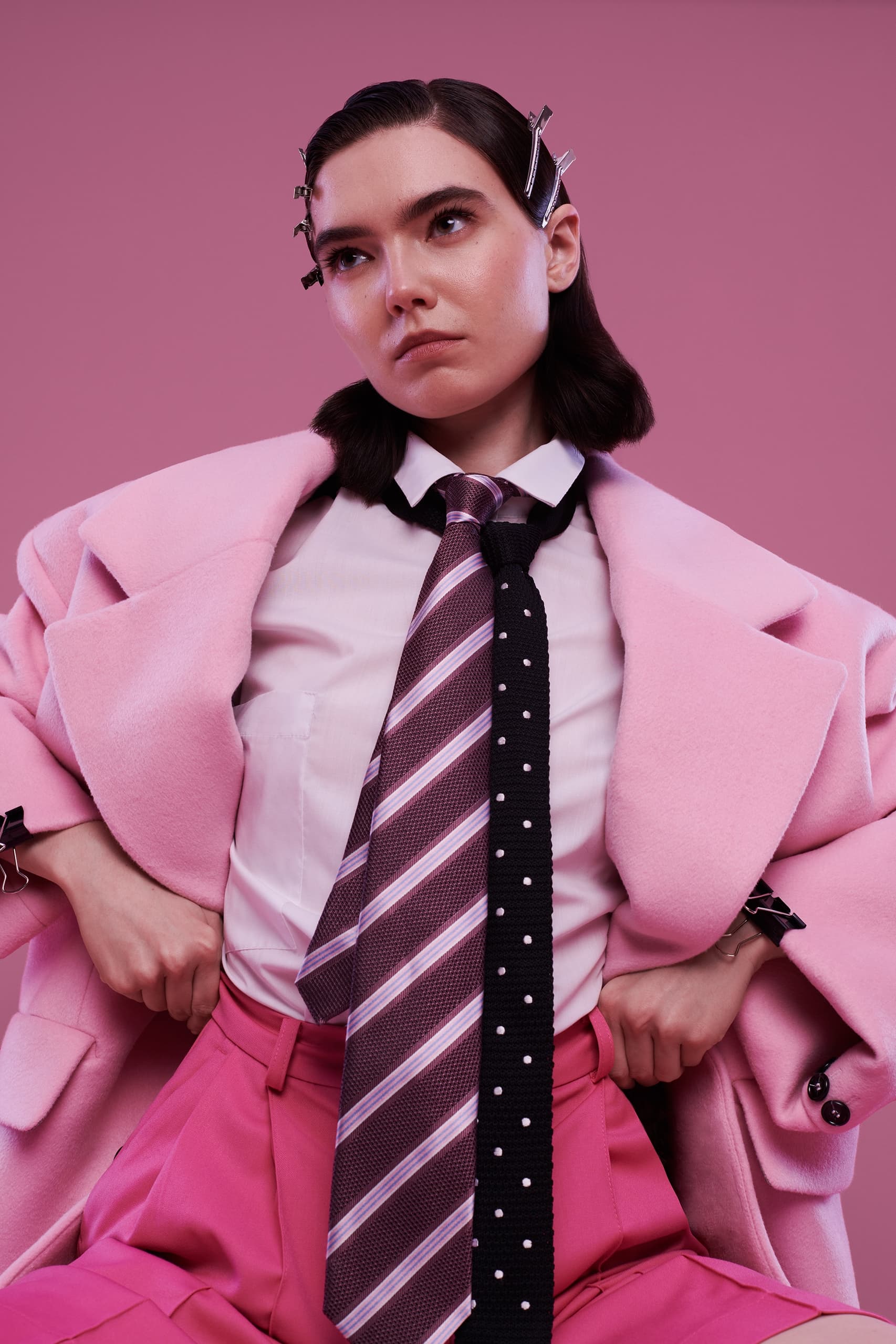 Fashion-forward individual wearing bold pink outfit and stylish ties against pink backdrop.