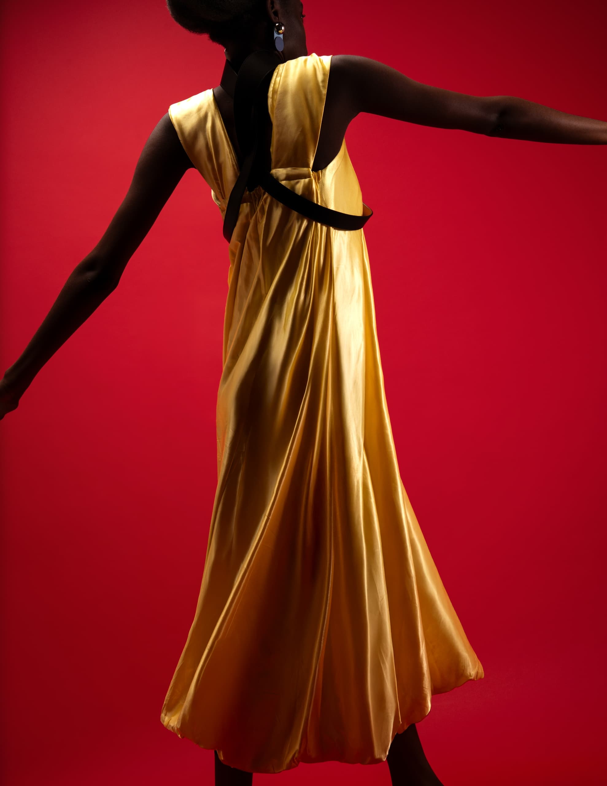 Elegant model in flowing yellow dress against vibrant red background.