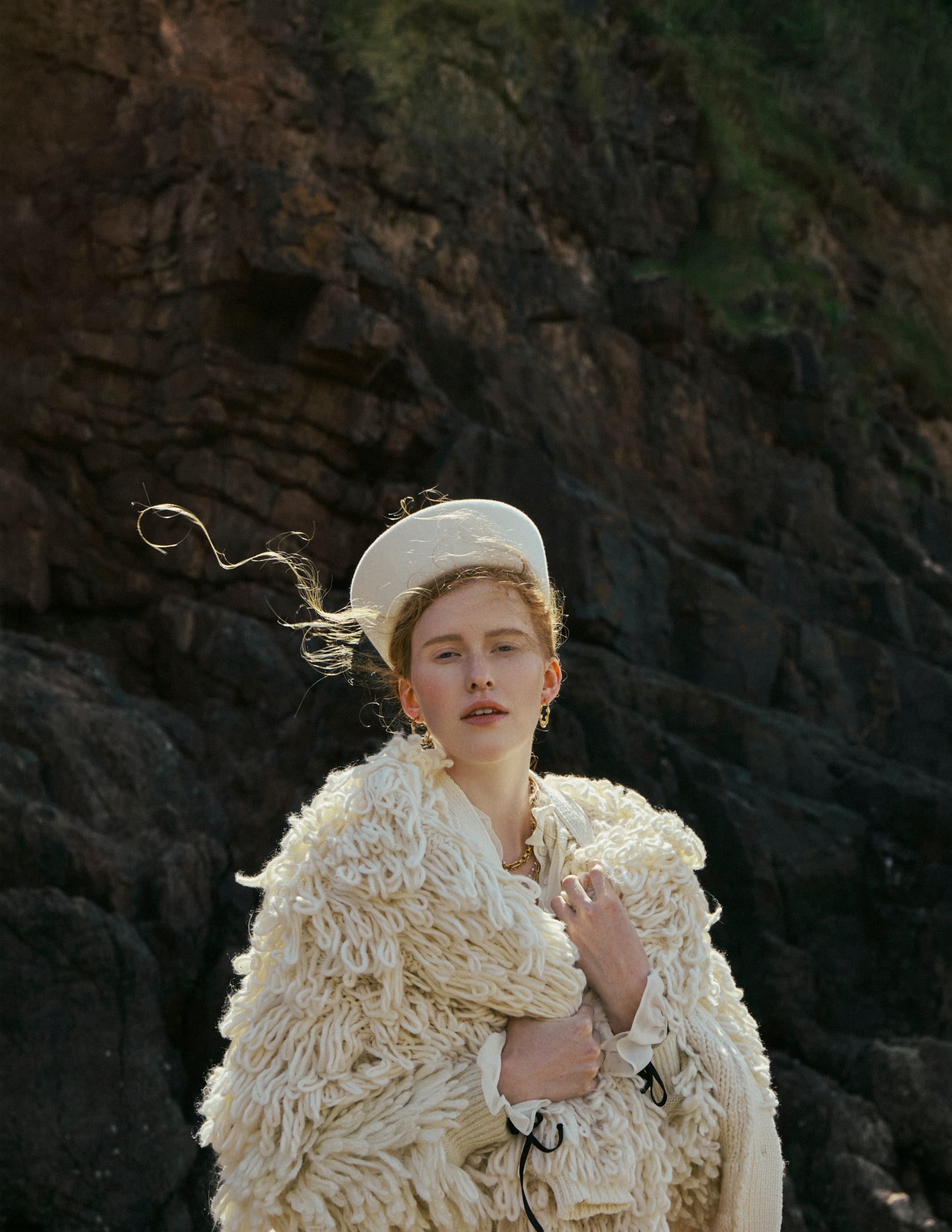 Person in textured white coat and hat standing against rocky background.