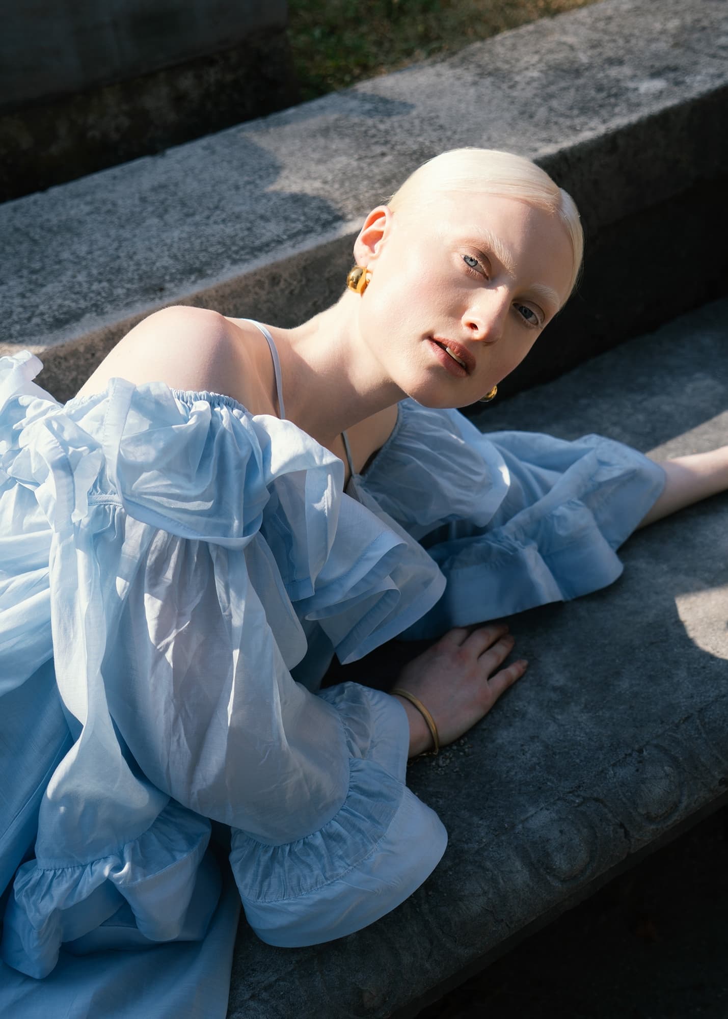 Woman in blue dress lying outdoors, sunlight casting shadows.