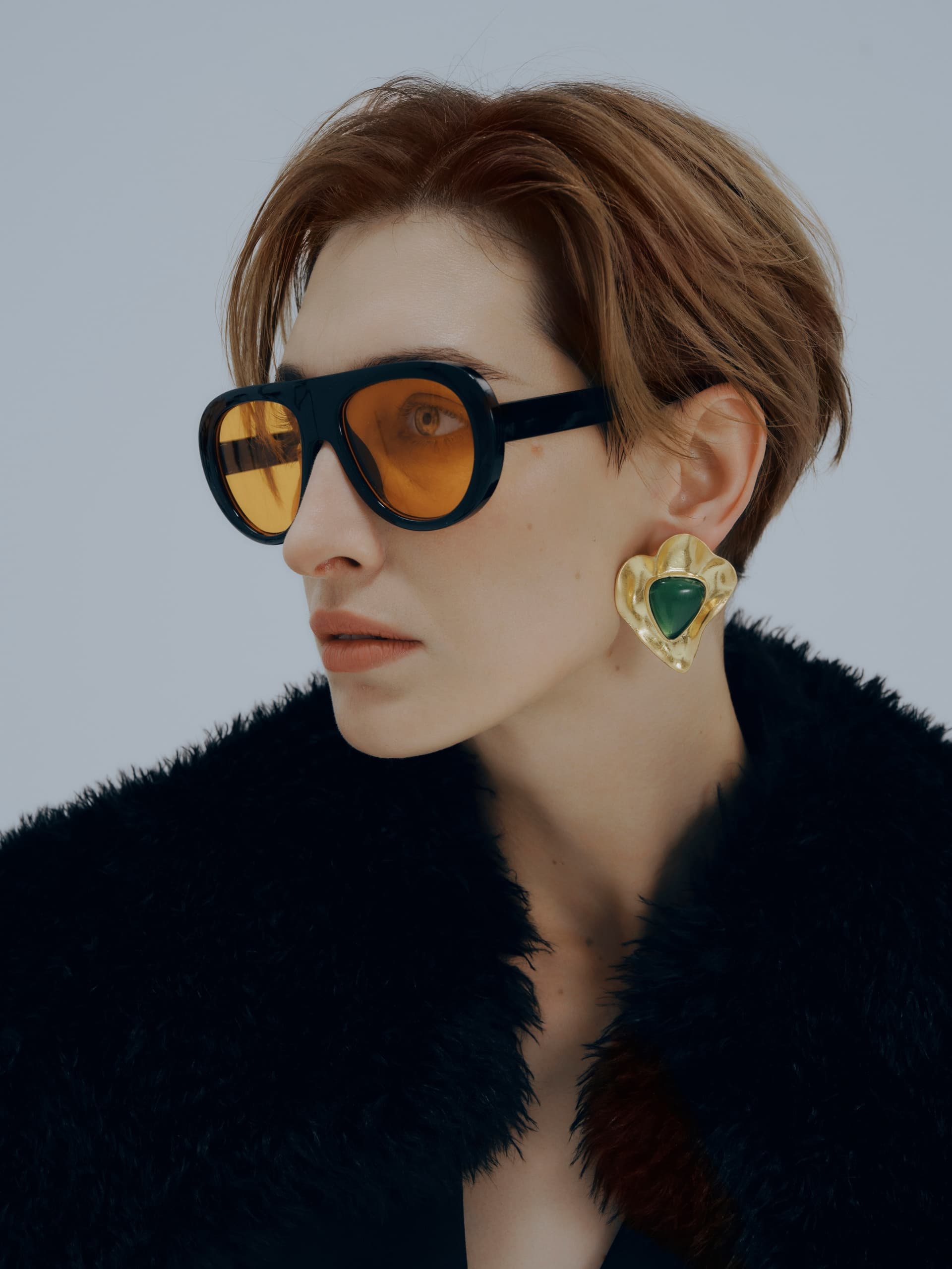 Stylish woman in orange sunglasses and fur coat with elegant earrings.
