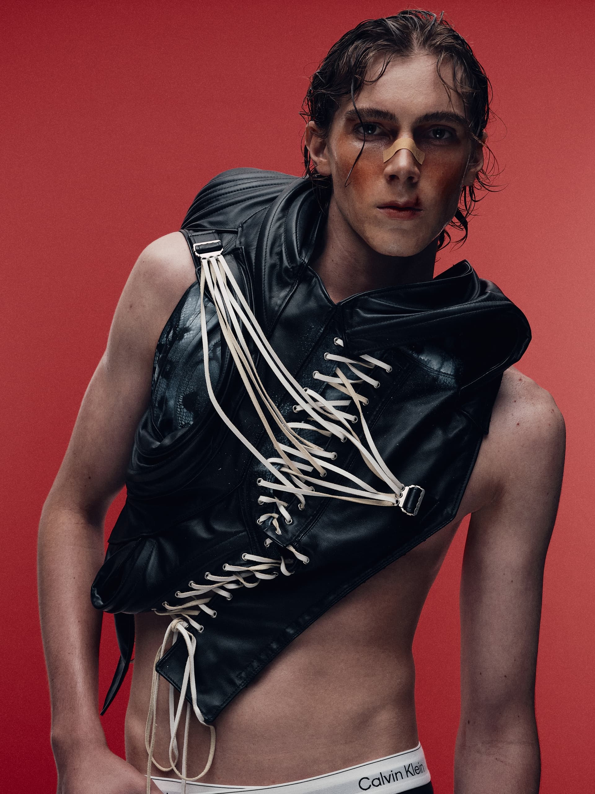 Fashion-forward model in edgy black leather and laces against a bold red background.