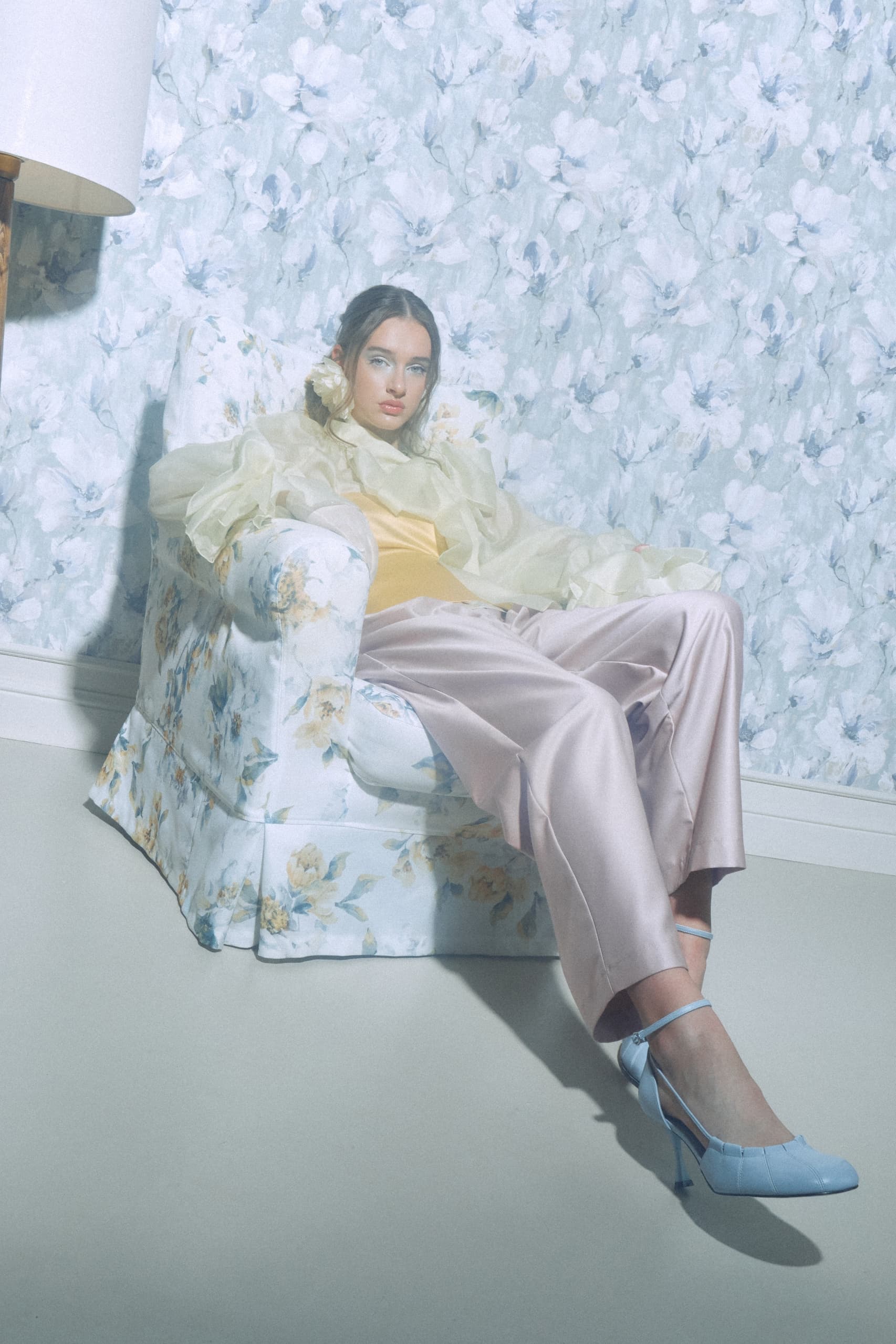 Woman in pastel fashion sits on floral chair.