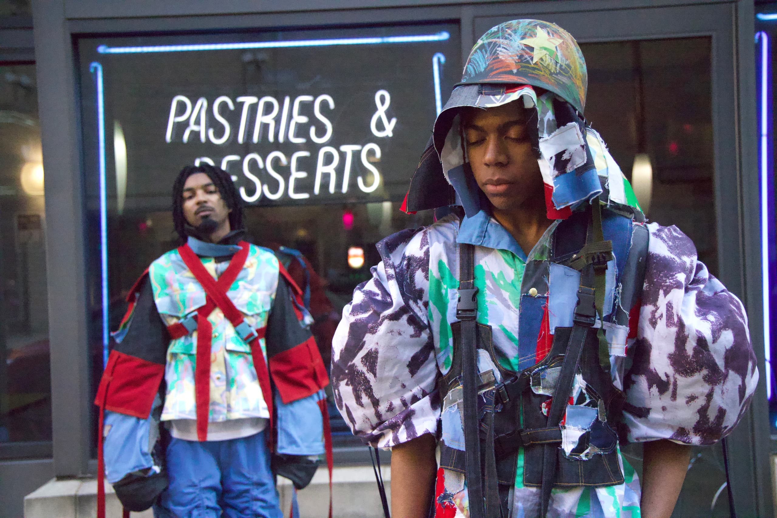 Two models in eclectic street fashion outside a pastries and desserts shop.