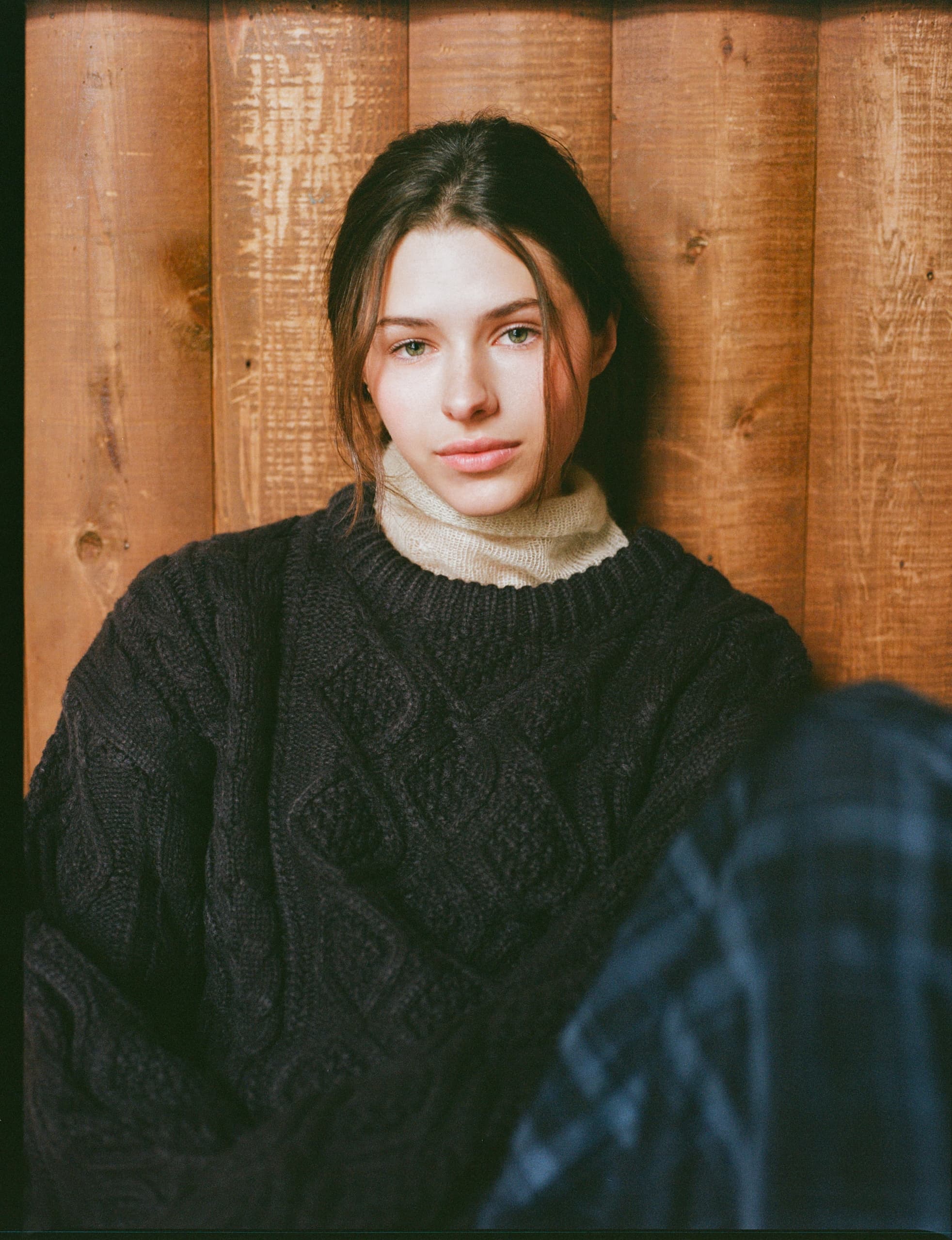 Portrait of a woman in a cozy sweater sitting against a wooden backdrop.