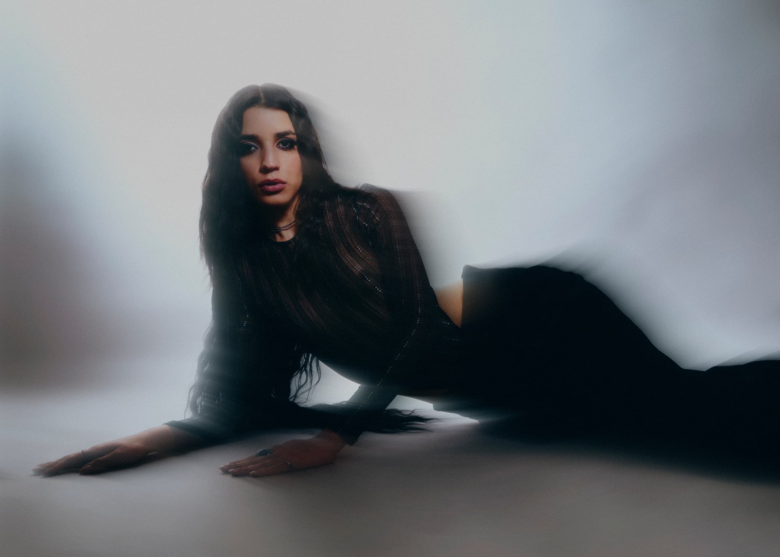 Woman posing elegantly in sheer striped top and pants, with a soft, blurred effect.